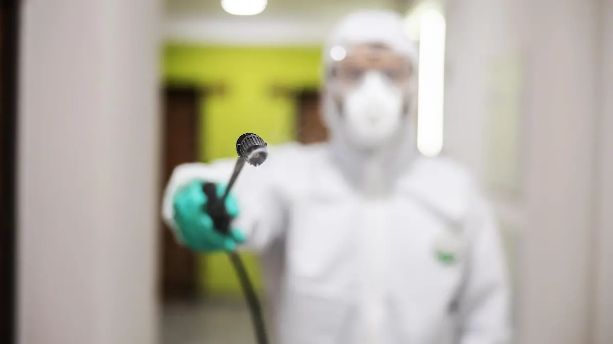 Closeup of worker in protective suit and mask sterilizing building. Selective focus on spray. Protection of corona virus / covid-19 concept. Selective focus on sprayer.