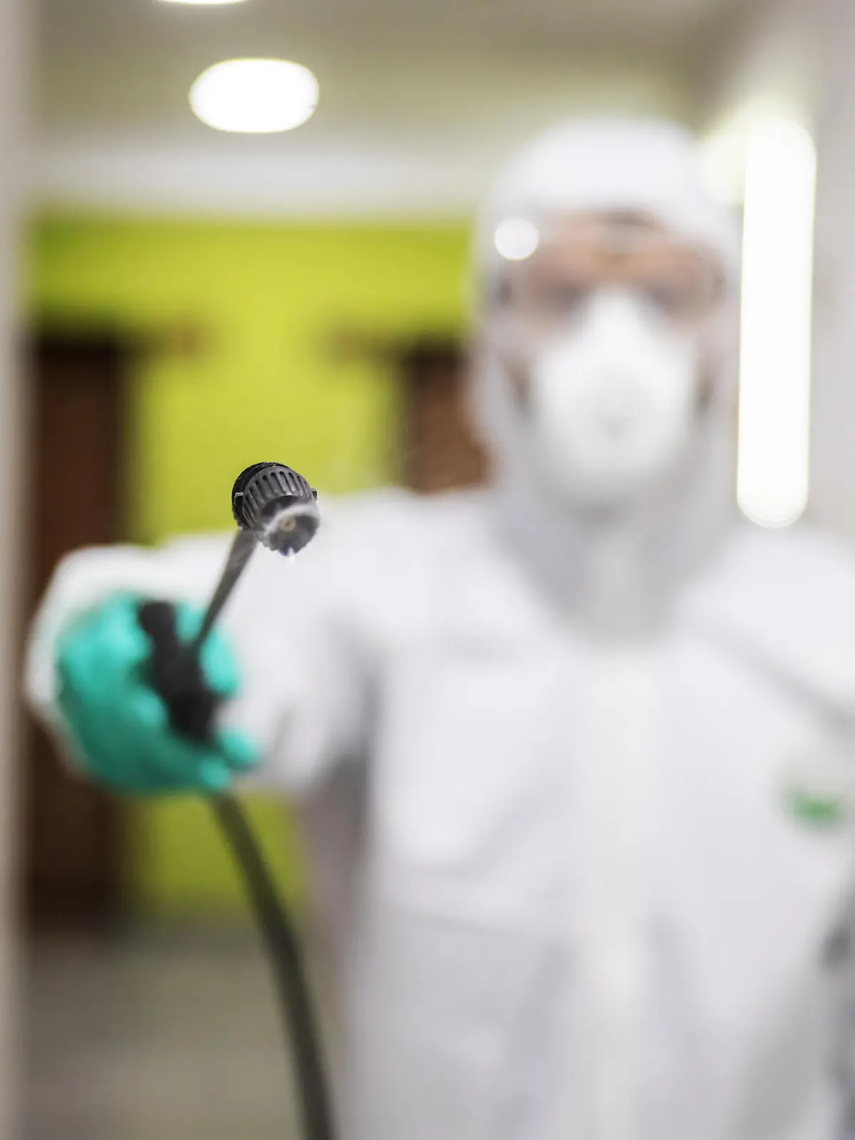 Closeup of worker in protective suit and mask sterilizing building. Selective focus on spray. Protection of corona virus / covid-19 concept. Selective focus on sprayer.