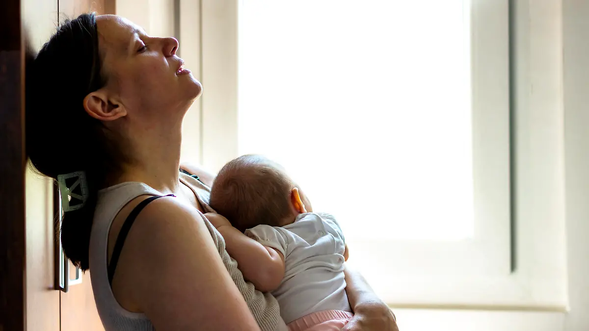 Mother embracing her baby girl while sleeping,lifestyle concept.Tired concerned mother rocking sleeping baby in kitchen.Portrait of young woman and cute little baby in home interior.Motherhood concept
