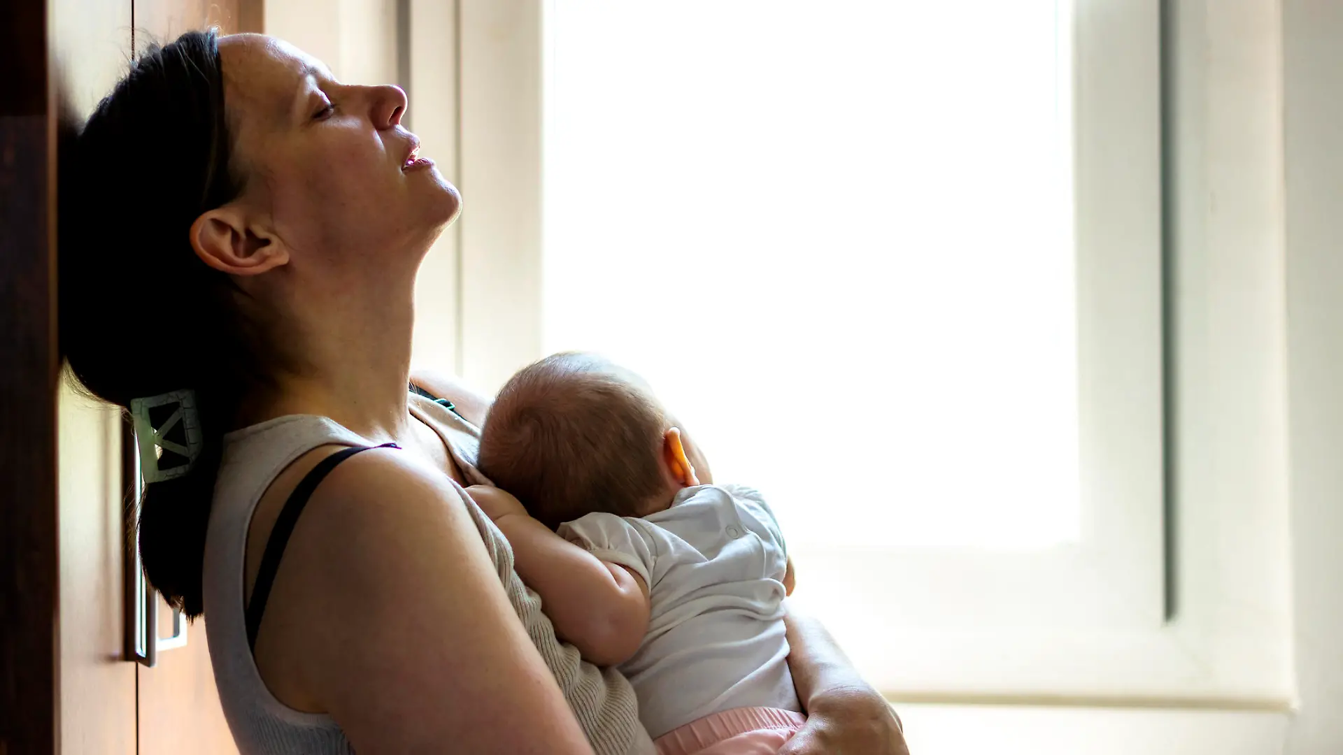 Mother embracing her baby girl while sleeping,lifestyle concept.Tired concerned mother rocking sleeping baby in kitchen.Portrait of young woman and cute little baby in home interior.Motherhood concept