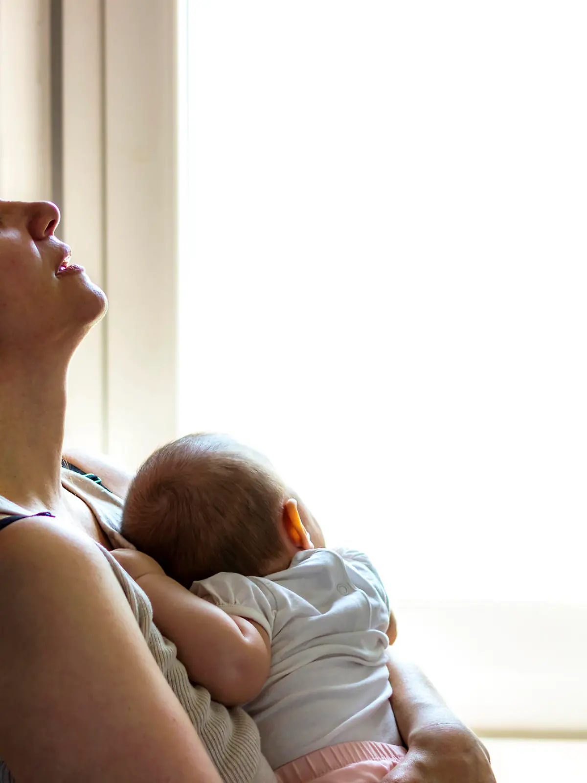 Mother embracing her baby girl while sleeping,lifestyle concept.Tired concerned mother rocking sleeping baby in kitchen.Portrait of young woman and cute little baby in home interior.Motherhood concept