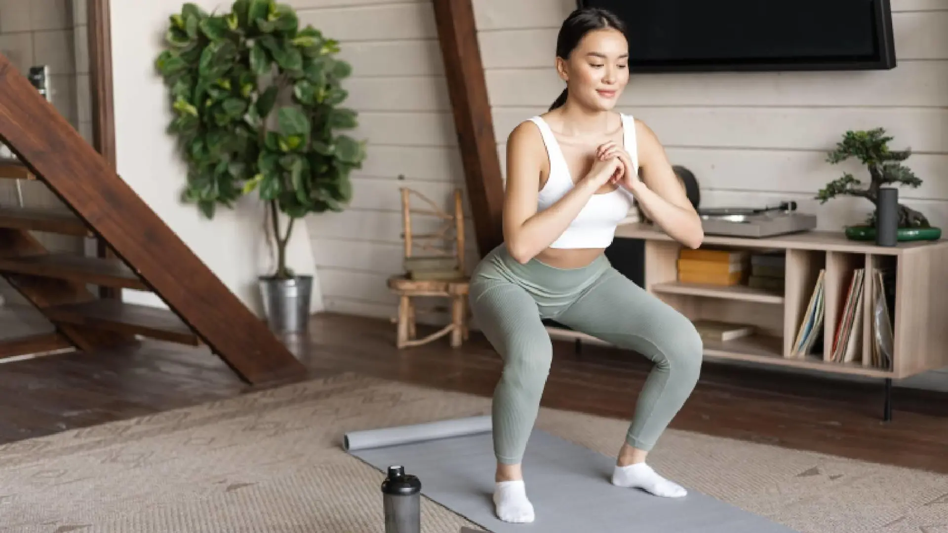 Young asian fitness girl doing squats workout at home, follow online sport gym instructor, standing on floor mat and smiling, doing exercises in living room.