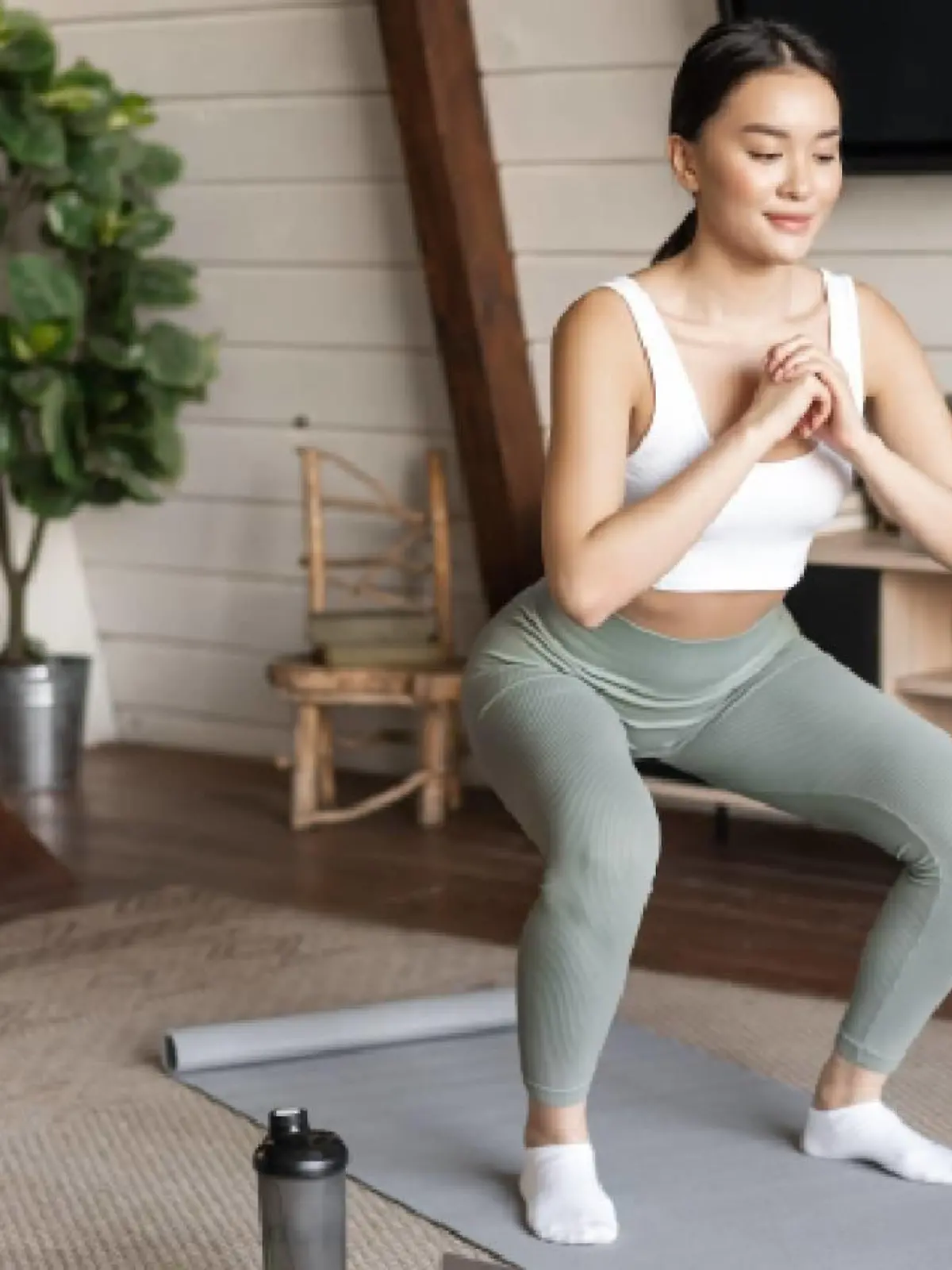 Young asian fitness girl doing squats workout at home, follow online sport gym instructor, standing on floor mat and smiling, doing exercises in living room.