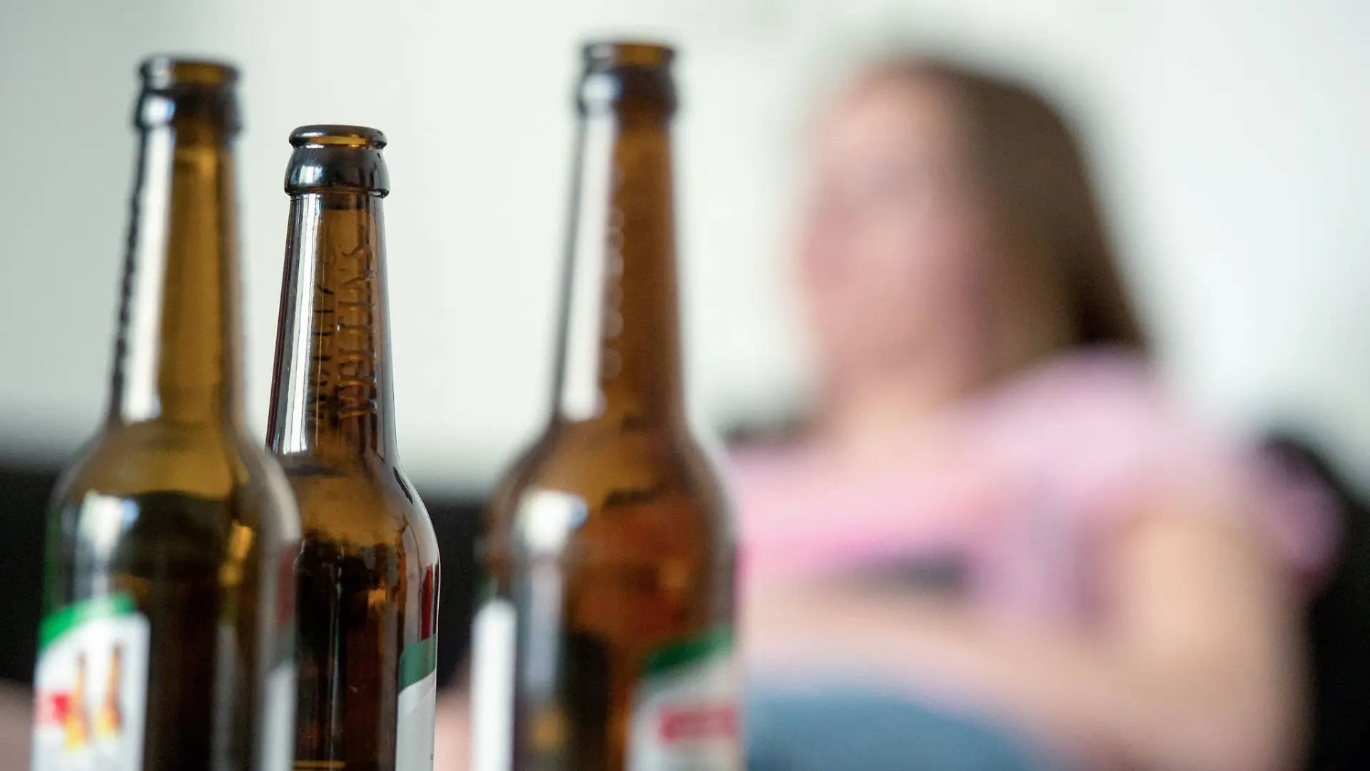 Eine junge Frau sitzt hinter leeren Bierflaschen.