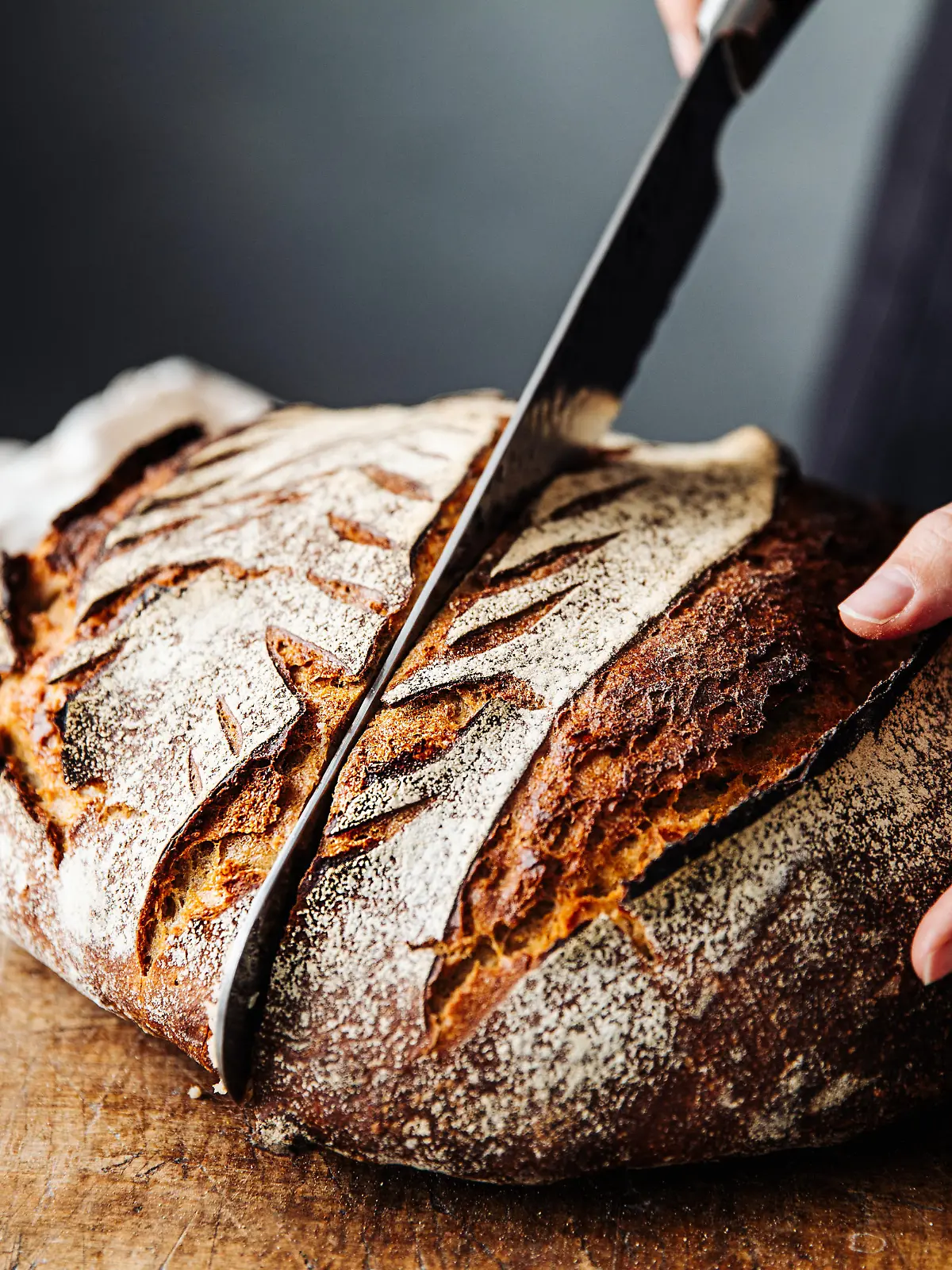Close-up of woman cutting sourdough bread on board. Midsection of female is with knife and baked bread. She is in kitchen.