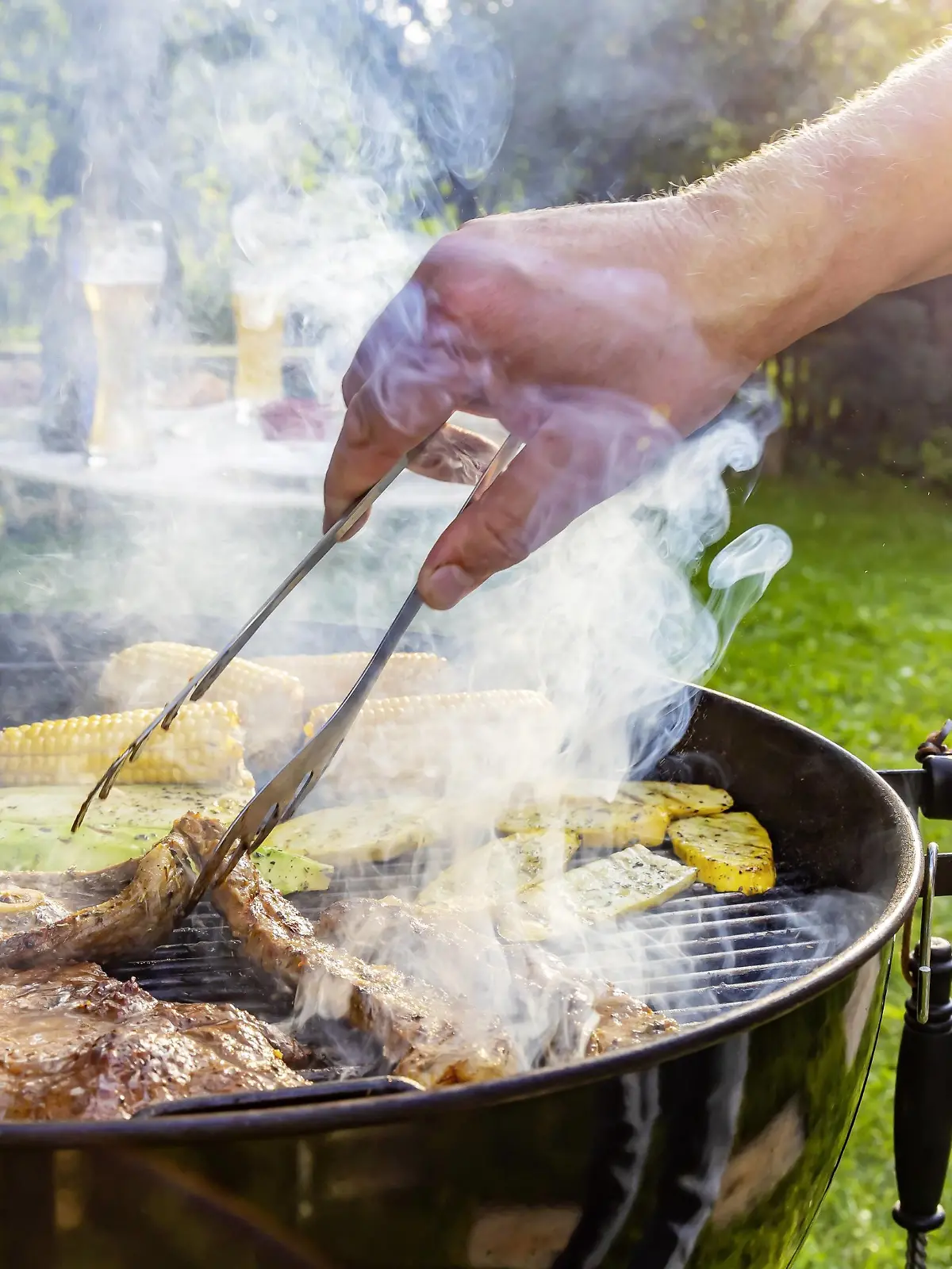 DEU, Deutschland, Münsingen, Baden-Württemberg, 24.08.2019: Grillfest im Garten. Auf dem Rost liegen Steaks vom Rind, Lammkeule, Schweinenacken sowie Tomaten, Mais und Zucchini. *** DEU, Germany, Münsingen, Baden Württemberg, 24 08 2019 Barbecue in the garden Steaks of beef, leg of lamb, neck of pork, tomatoes, corn and courgettes lie on the grill  