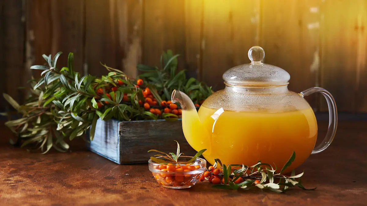 Glass teapot and sea buckthorn tea cup on wooden background. Cozy autumn composition. Long wide banner