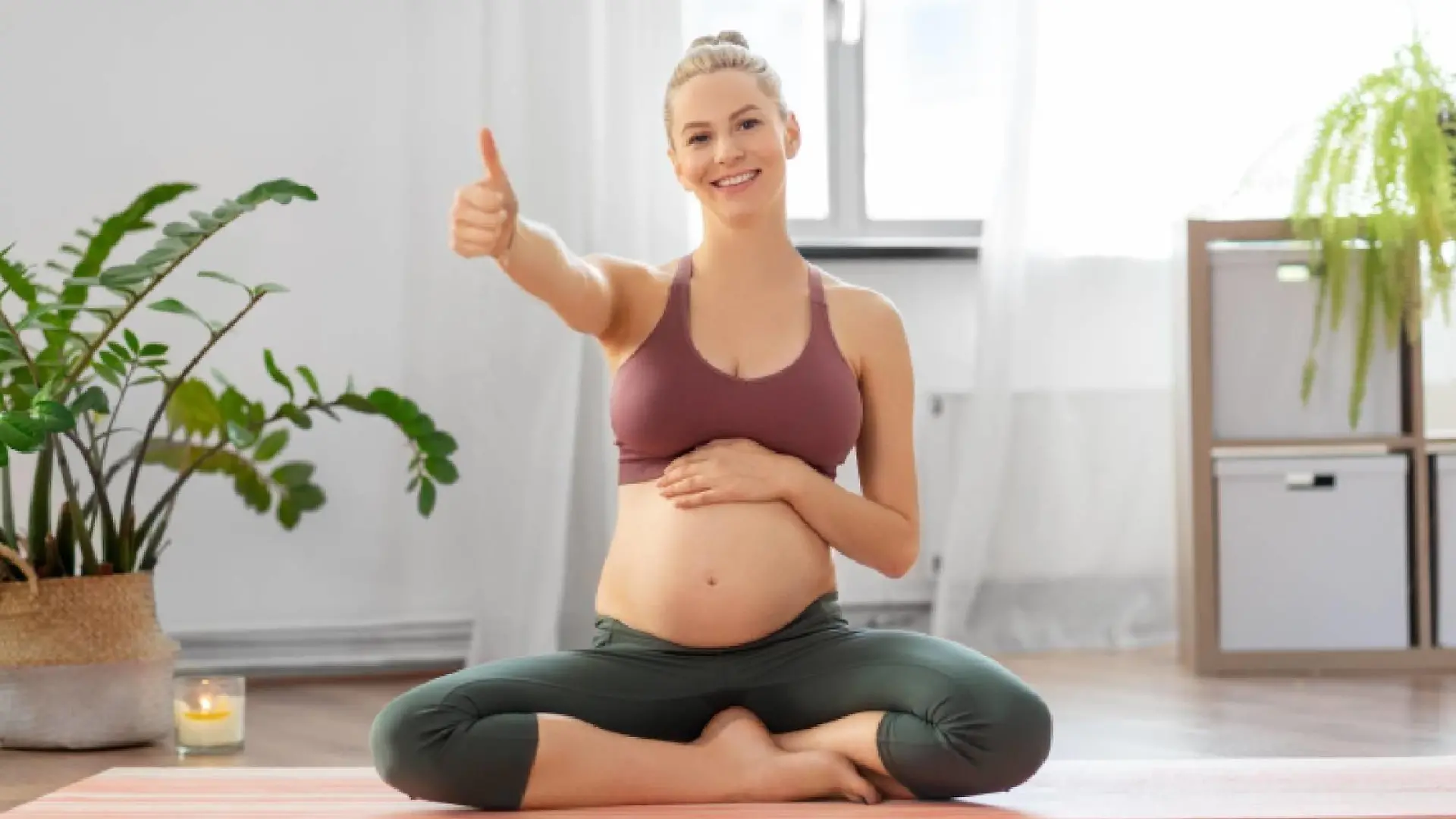 fitness, sport and people concept - happy pregnant woman showing thumbs up sitting on yoga mat at home