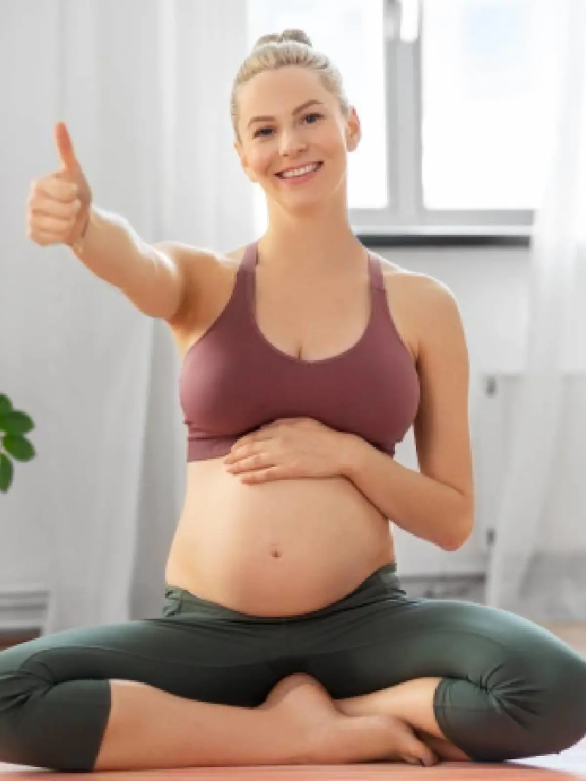 fitness, sport and people concept - happy pregnant woman showing thumbs up sitting on yoga mat at home