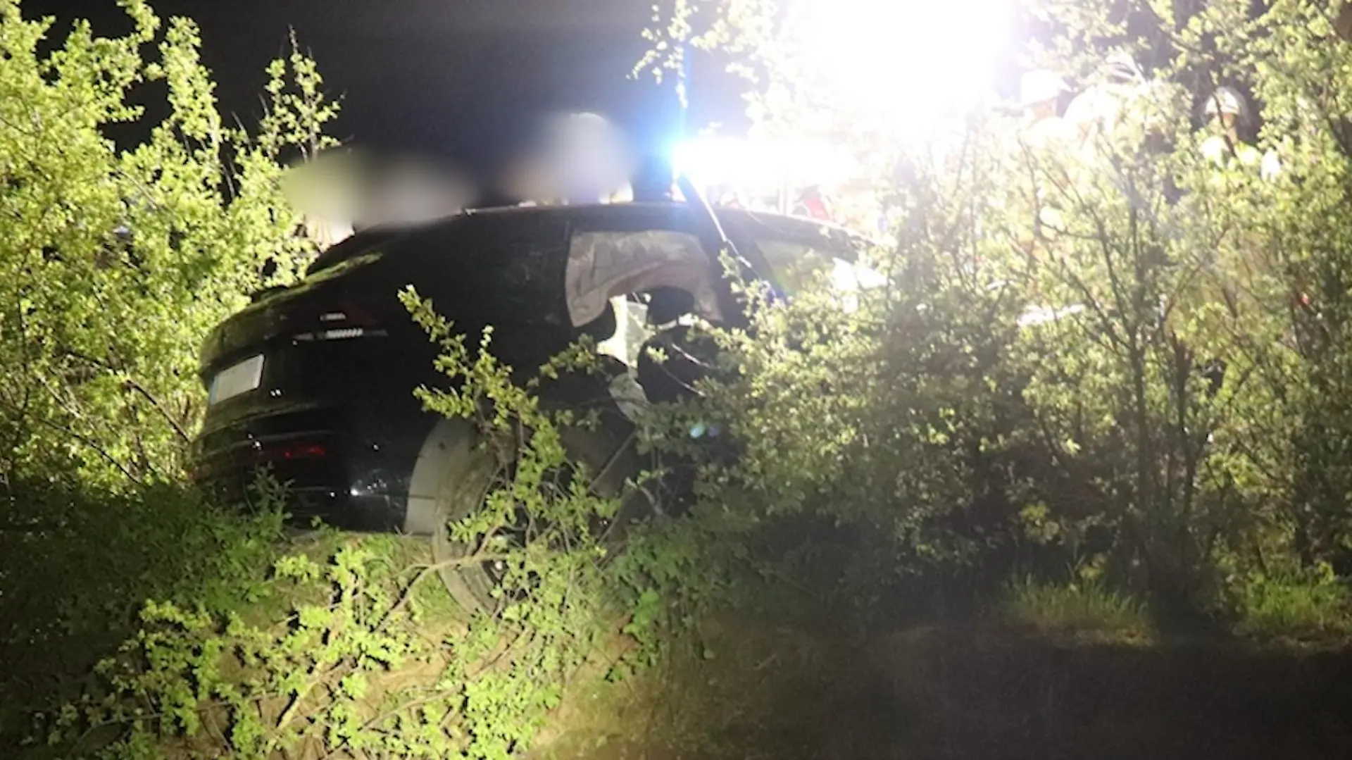 Ein verunfalltes Auto in einer Böschung, dahinter Einsatzkräfte.