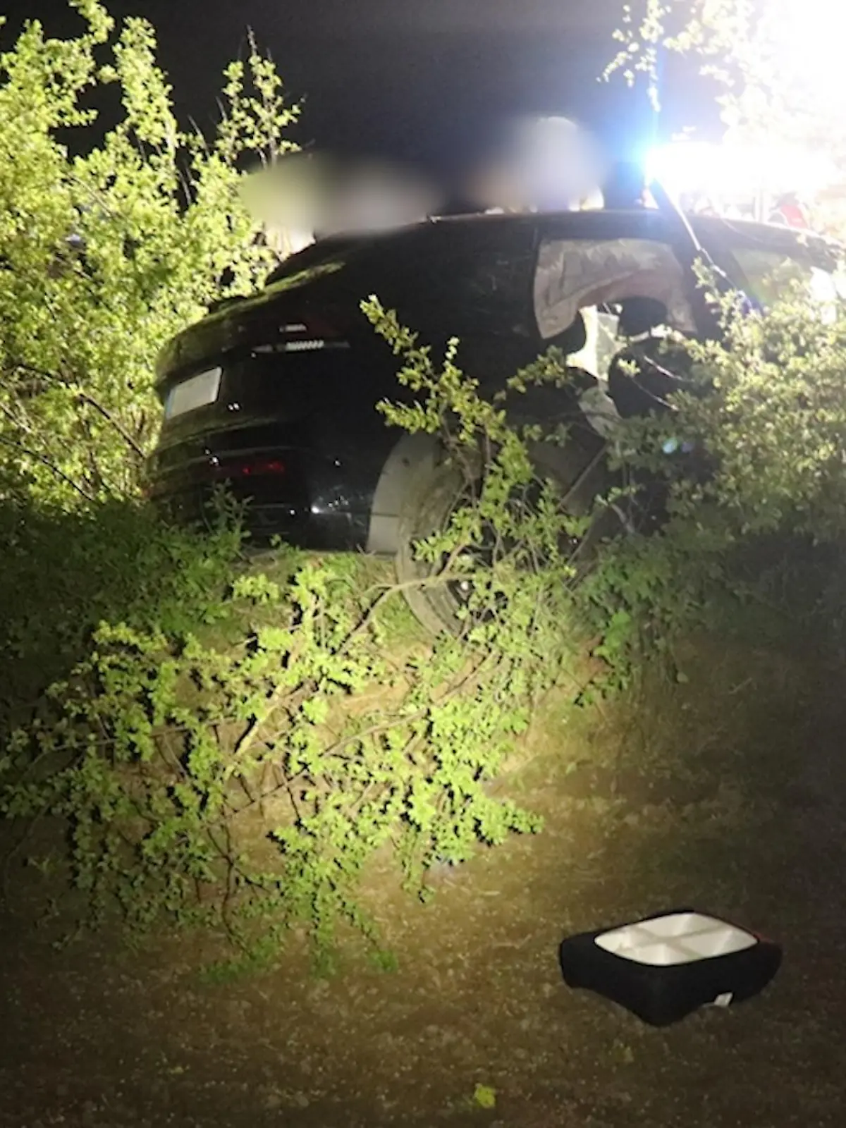 Ein verunfalltes Auto in einer Böschung, dahinter Einsatzkräfte.