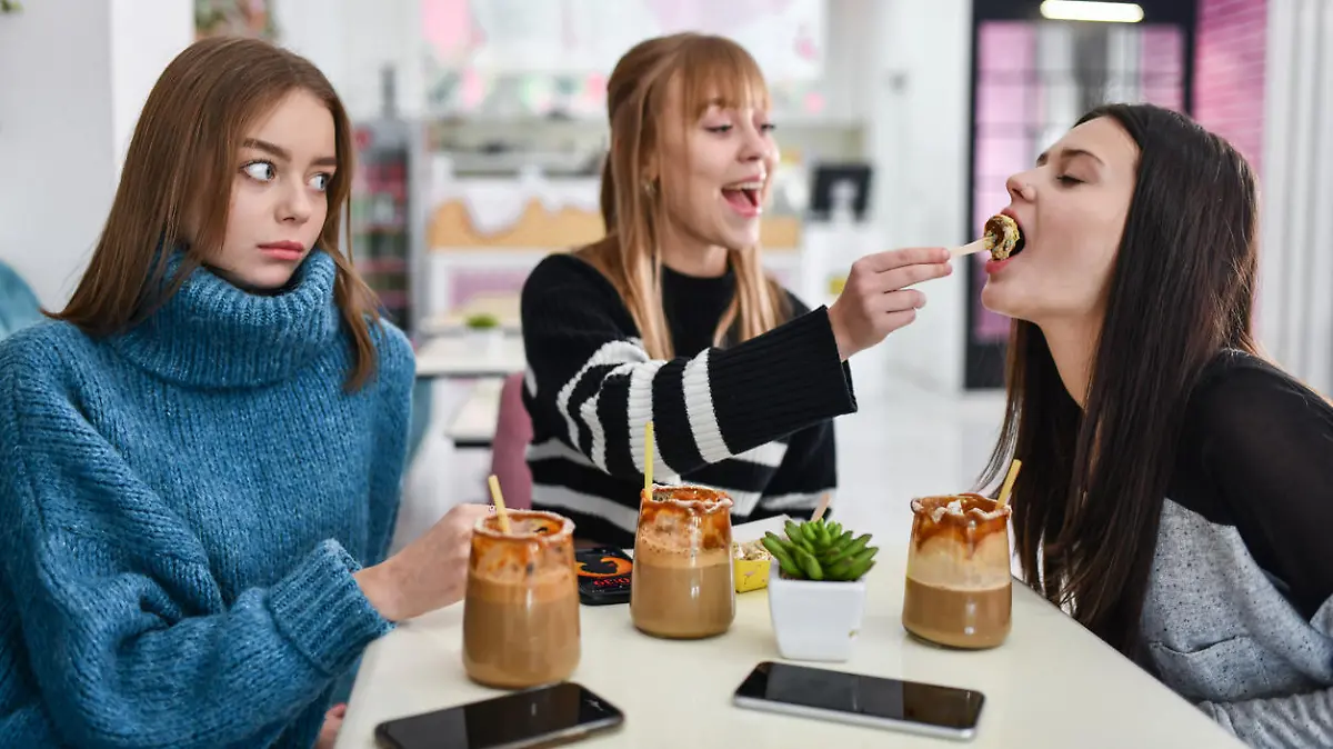 Female Looking Surprised At Two Friends Feeding Each Other Poffertjes In Restaurant
