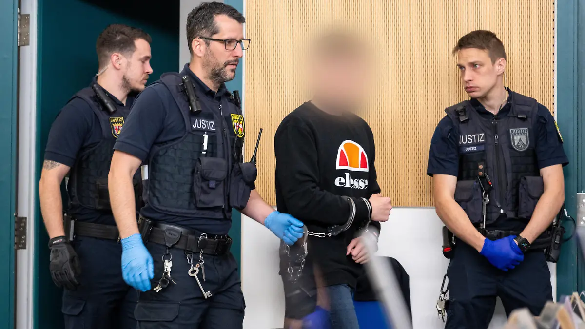 15.04.2024, Rheinland-Pfalz, Trier: Justizbedienstete bringen einen Angeklagten wegen gemeinschaftlichem Mord in den Gerichtssaal. Der Jugendliche soll mit einem Bekannten und dessen Mutter einen Arzt aus der Eifel getötet haben. Foto: Harald Tittel/dpa - ACHTUNG: Person wurde aus rechtlichen Gründen gepixelt +++ dpa-Bildfunk +++