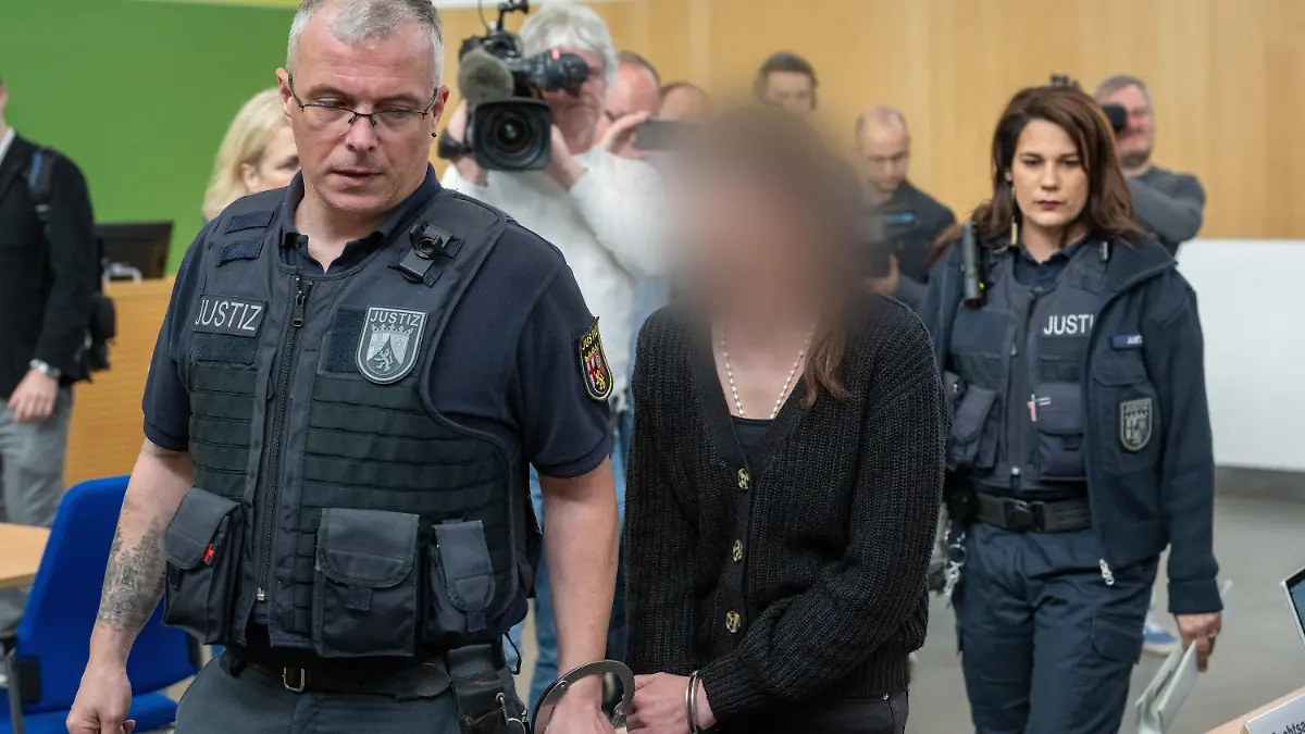 15.04.2024, Rheinland-Pfalz, Trier: Die Lebensgefährtin (M) eines Gerolsteiner Arztes wird von Justizbediensteten zur Anklagebank geführt. Sie ist wegen gemeinschaftlichem Totschlag angeklagt. Ihr Sohn und ein weiterer Jugendlicher ist wegen gemeinschaftlichem Mord angeklagt. Foto: Harald Tittel/dpa - ACHTUNG: Person wurde aus rechtlichen Gründen gepixelt +++ dpa-Bildfunk +++