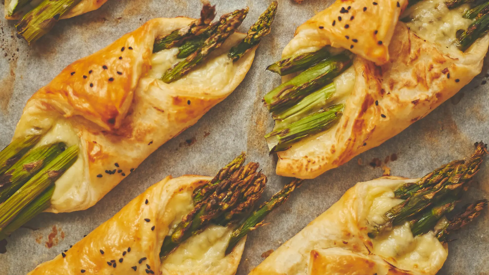 Baked green asparagus in puff pastry sprinkled with sesame seeds and cheese. Placed on a white baking paper background. Close-up, top view, flat lay.
