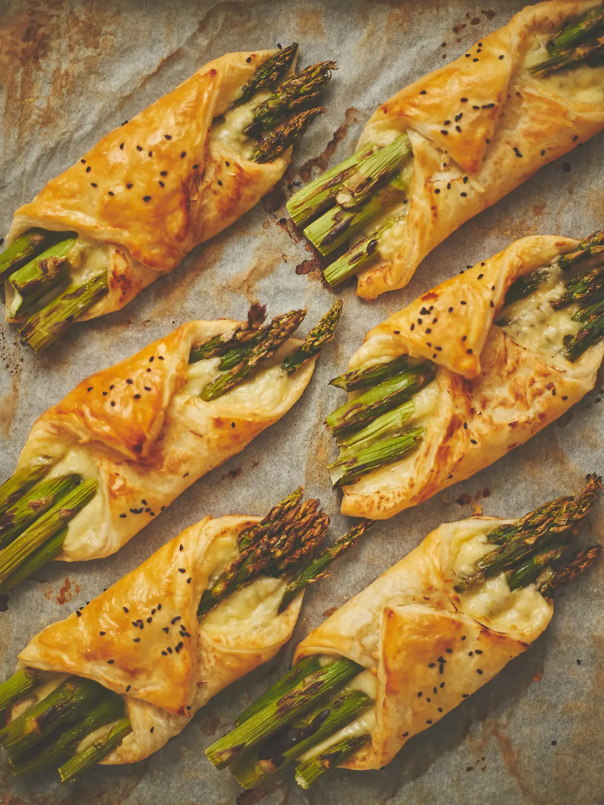 Baked green asparagus in puff pastry sprinkled with sesame seeds and cheese. Placed on a white baking paper background. Close-up, top view, flat lay.