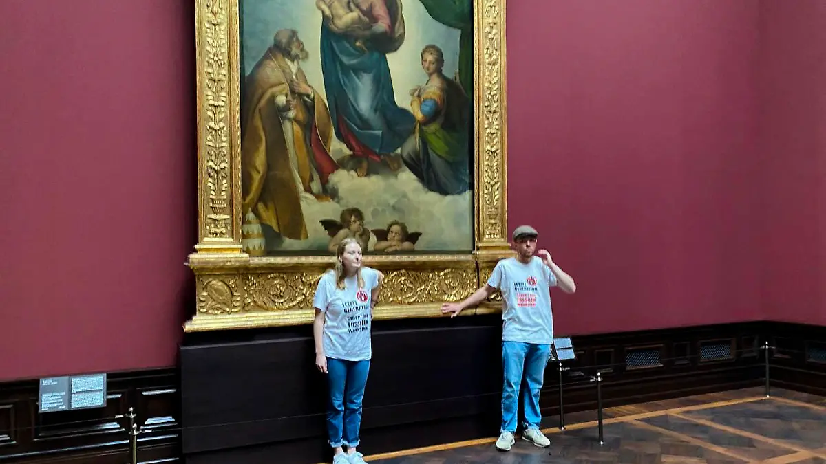 In this photo provided by the climate activist group 'Letzte Generation', Last Generation, shows activist glued themselves to the frame of the painting 'Sistine Madonna' by Raffael at the Gemaeldegalerie Museum in Dresden, Germany, Tuesday, Aug. 23, 2022. (Letzte Generation via AP)
