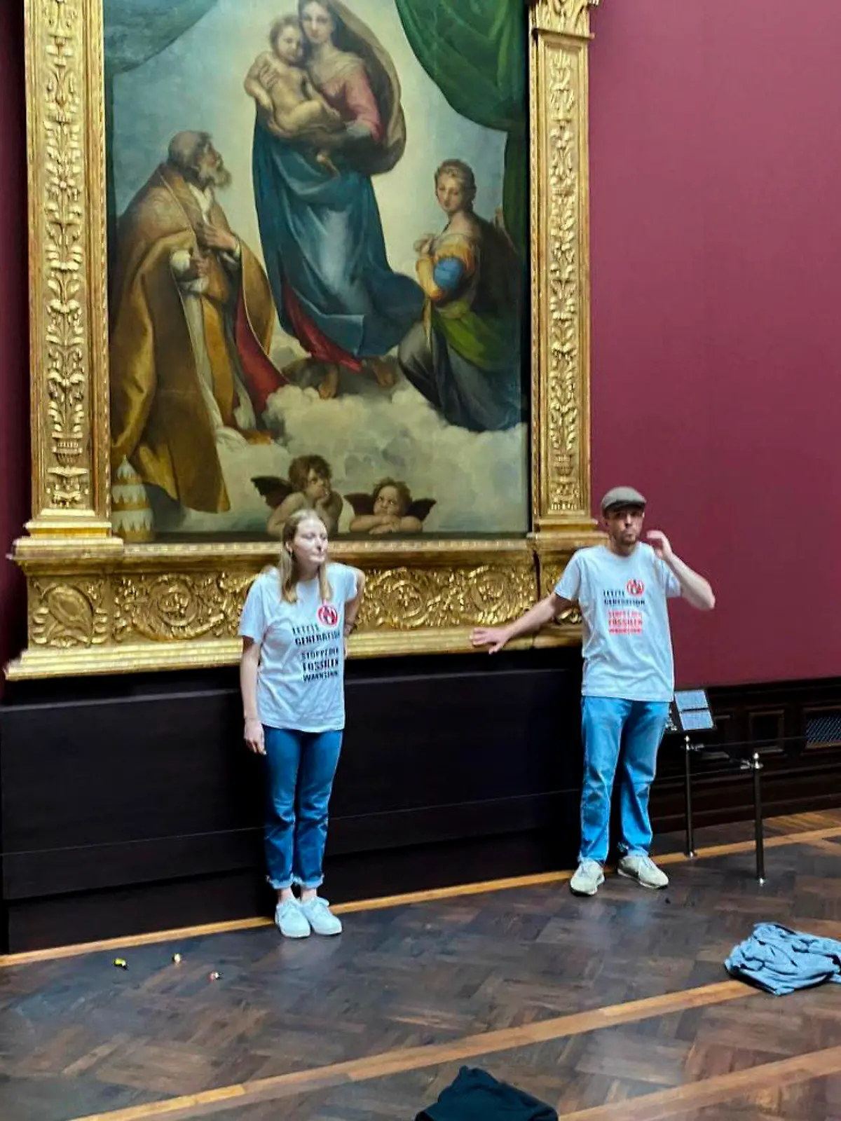In this photo provided by the climate activist group 'Letzte Generation', Last Generation, shows activist glued themselves to the frame of the painting 'Sistine Madonna' by Raffael at the Gemaeldegalerie Museum in Dresden, Germany, Tuesday, Aug. 23, 2022. (Letzte Generation via AP)