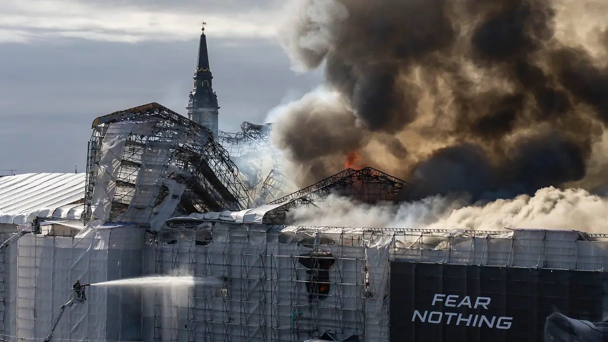 16.04.2024, Dänemark, Kopenhagen: Feuerwehrleute arbeiten neben dem Schriftzug «Fear nothing» (fürchte nichts), während Rauch aus der Alten Börse («Boersen») aufsteigt. Eines der ältesten Gebäude Kopenhagens steht in Flammen, und seine ikonische Turmspitze ist eingestürzt. Das Dach der alten Börse (Boersen) aus dem 17. Jahrhundert, die einst das Finanzzentrum Dänemarks war, wurde am Dienstag von Flammen zerstört. Foto: Emil Nicolai Helms/Ritzau Scanpix Foto/AP +++ dpa-Bildfunk +++
