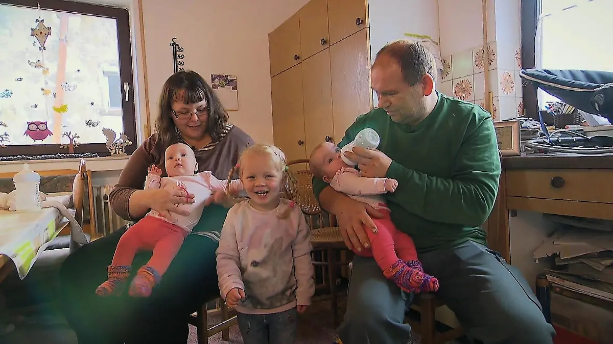 Lina lacht während sie zwischen ihren neuen Schwestern steht, die gerade gefüttert werden.