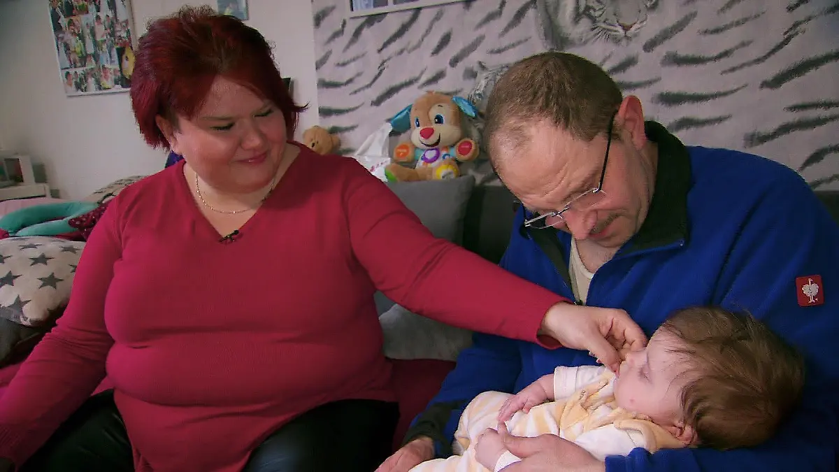 Steffen und Nicole kuscheln mit ihrer Tochter auf dem Sofa.