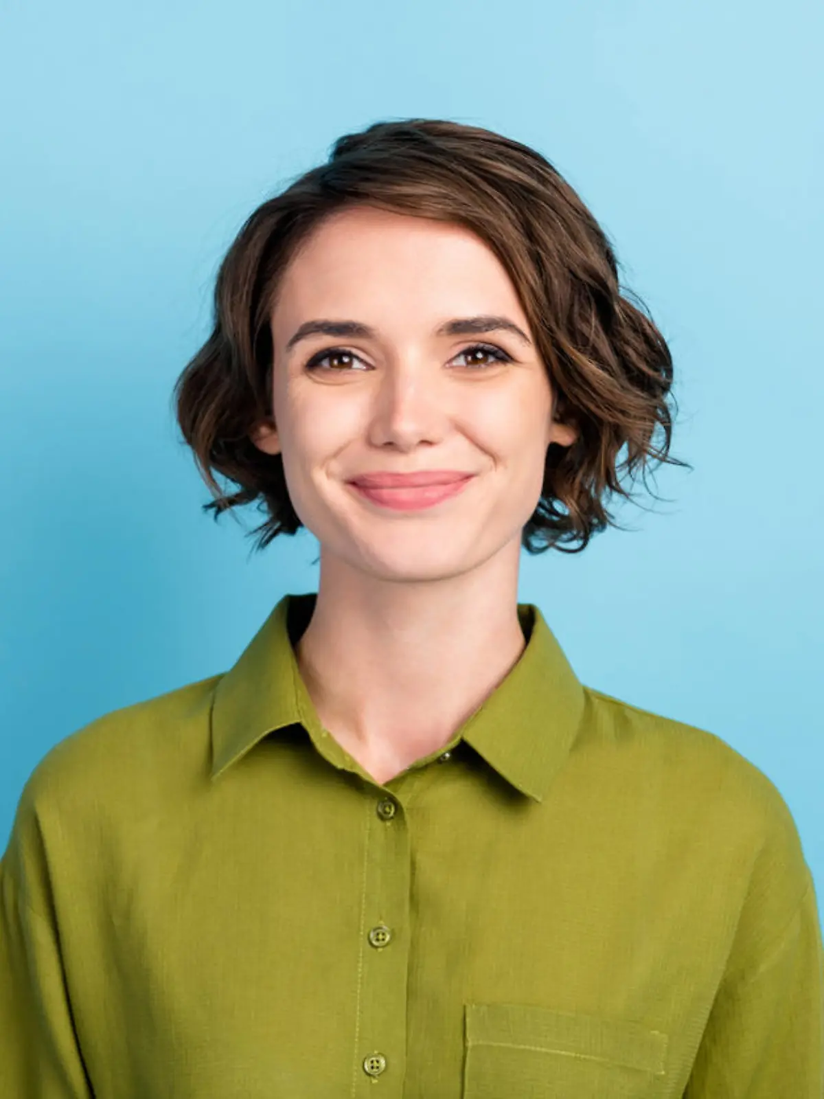 Photo portrait of cute smiling pretty girl with brunette short hair wearing green shirt, isolated on blue color background