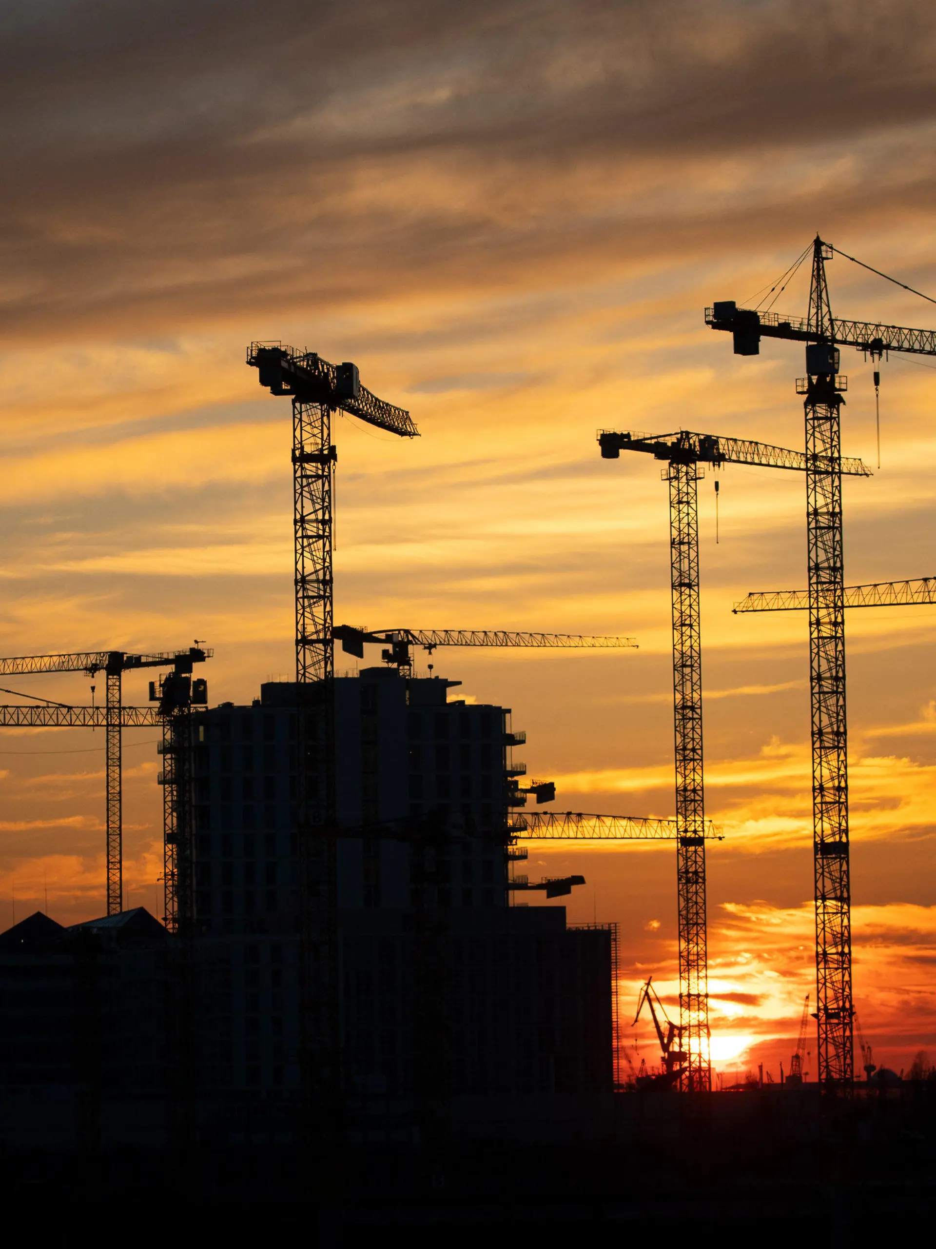 ARCHIV - 25.03.2020, Hamburg: Die Kräne verschiedener Baustellen in der Hafencity zeichnen sich im Sonnenuntergang ab. Wie sich die Finanzen von Bund, Ländern, Gemeinden und Sozialversicherung im ersten Halbjahr 2022 entwickelt haben, gibt das Statistische Bundesamt am Donnerstag bekannt. (zu dpa «Statistiker geben Daten zu Staatshaushalt und Konjunktur bekannt») Foto: Christian Charisius/dpa +++ dpa-Bildfunk +++