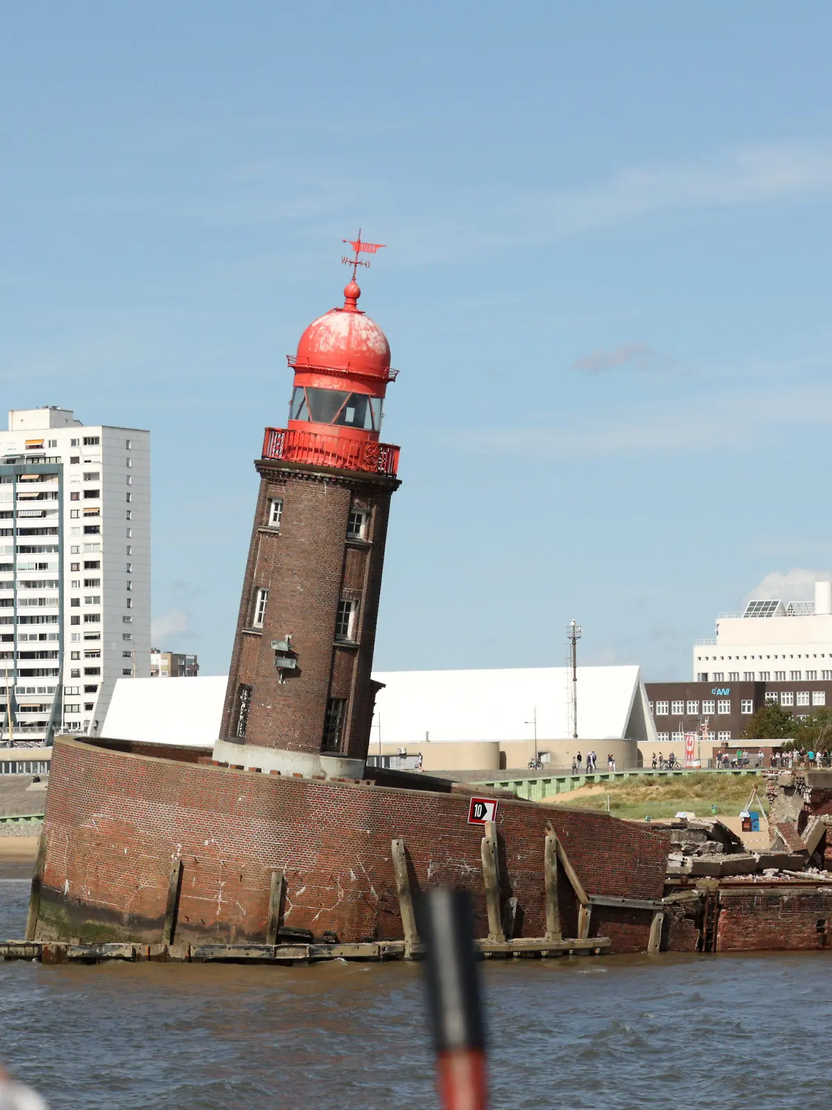 20.08.2022, Bremen, Bremerhaven: Schaulustige beobachten den abgesackten Moleturm in Bremerhaven. In der Nacht zum Donnerstag hatte sich die Nordmole, an deren Spitze das Leuchtfeuer mit dem roten Haupt steht, abgesenkt, wobei der rund 20 Meter hohe Turm in eine bedrohliche Schieflage geriet. Foto: Markus Hibbeler/dpa +++ dpa-Bildfunk +++