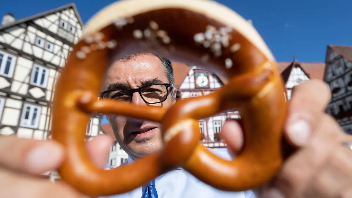 dpatopbilder - 25.08.2022, Baden-Württemberg, Bad Urach: Bundesernährungsminister Cem Özdemir (Bündnis 90/Die Grünen) zeigt auf dem Marktplatz seines Geburtsorts nach dem Besuch einer Bäckerei eine Brezel. Foto: Marijan Murat/dpa +++ dpa-Bildfunk +++
