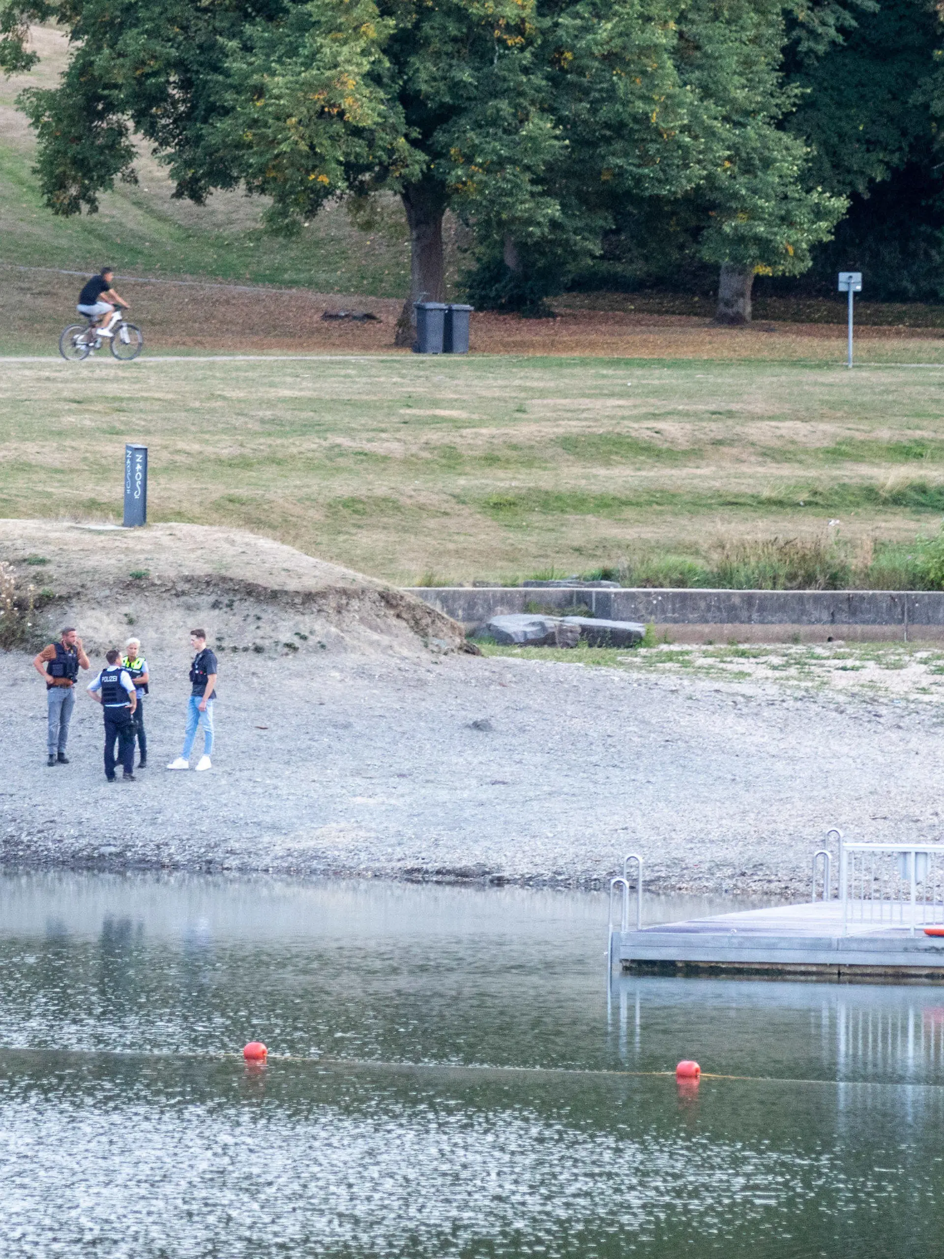 25.08.2022, Nordrhein-Westfalen, Simmerath: Polizisten stehen am Ufer des Eiserbachsees im Rurseezentrum. Nach einem Badeunfall in dem Badesee bei Aachen sind zwei Kinder gestorben. Das teilte eine Sprecherin der Polizei am 26.08. mit. Die sieben und neun Jahre alten Jungen waren laut Polizei am frühen Donnerstagabend am Eiserbachsee als vermisst gemeldet und dann wenig später leblos im Wasser gefunden worden. Foto: Ralf Roeger/dpa +++ dpa-Bildfunk +++