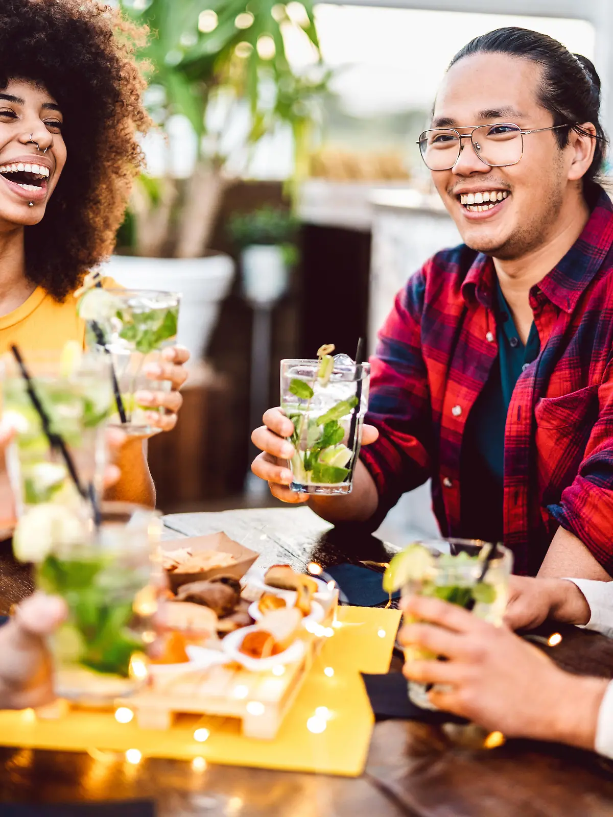 Young friends toasting mojito drinks at fashion cocktail pub restaurant - Life style concept with milenial people having drunk fun cheering on happy hour at bar
