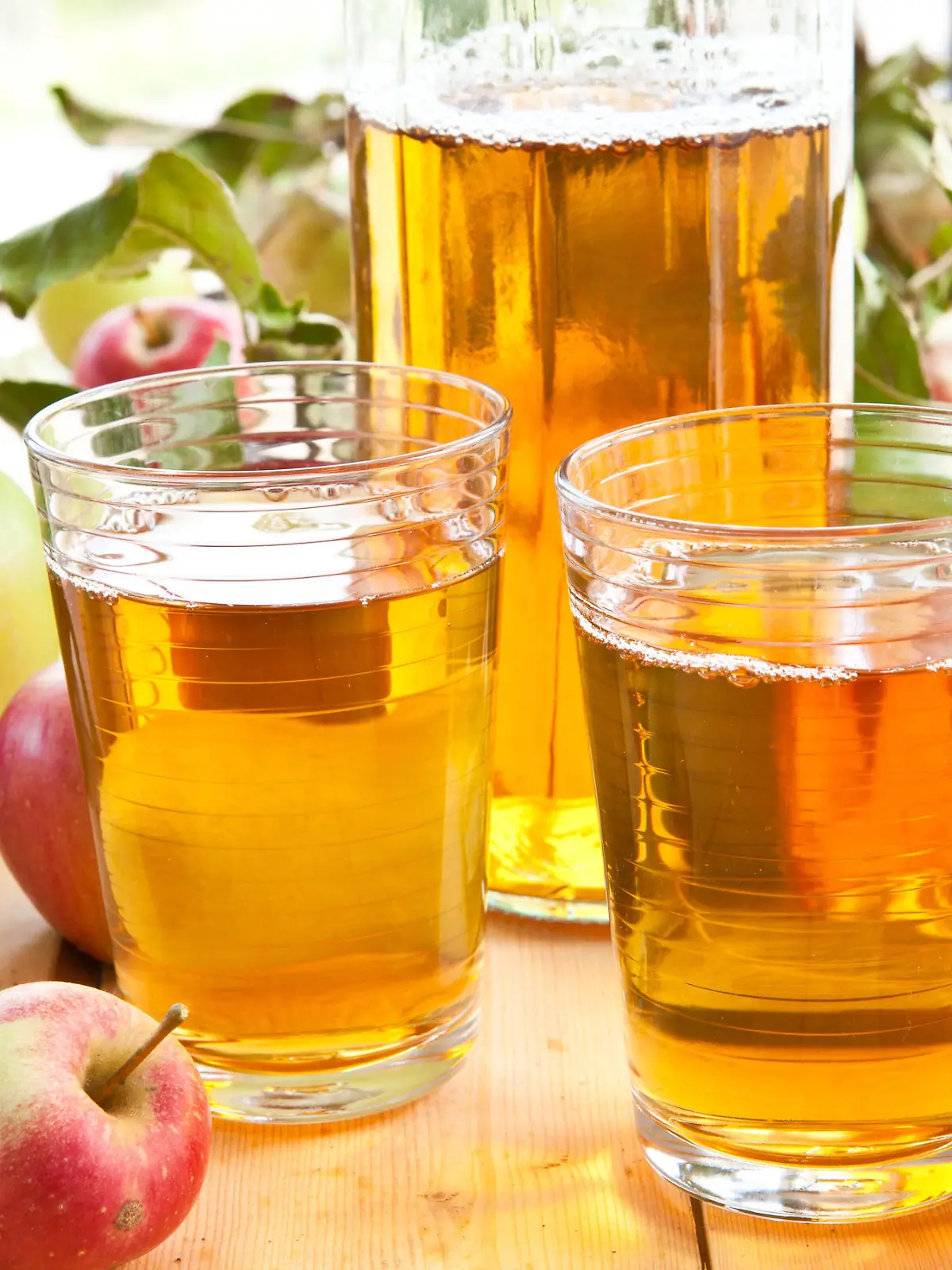 Apfelsaft in Krug und Gläsern, umgeben von Äpfeln