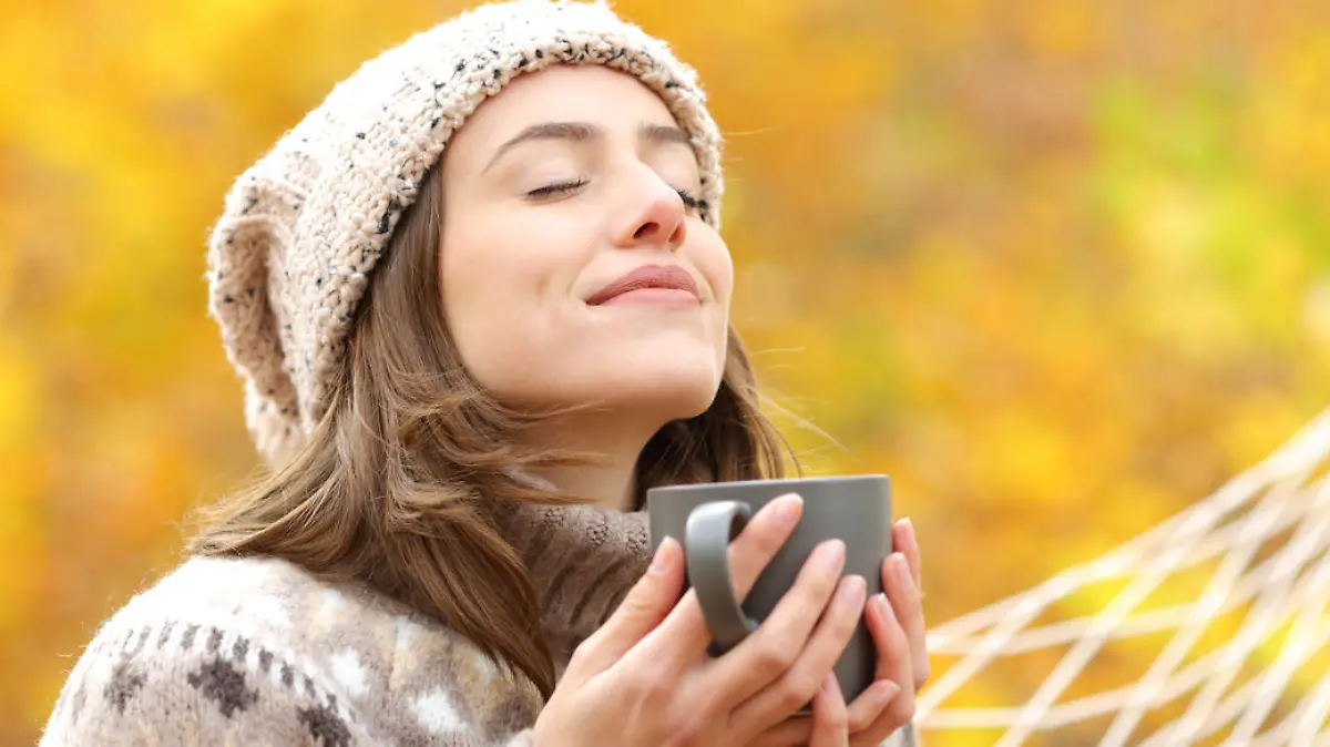 Woman breaths fresh air holding coffee cup in autumn