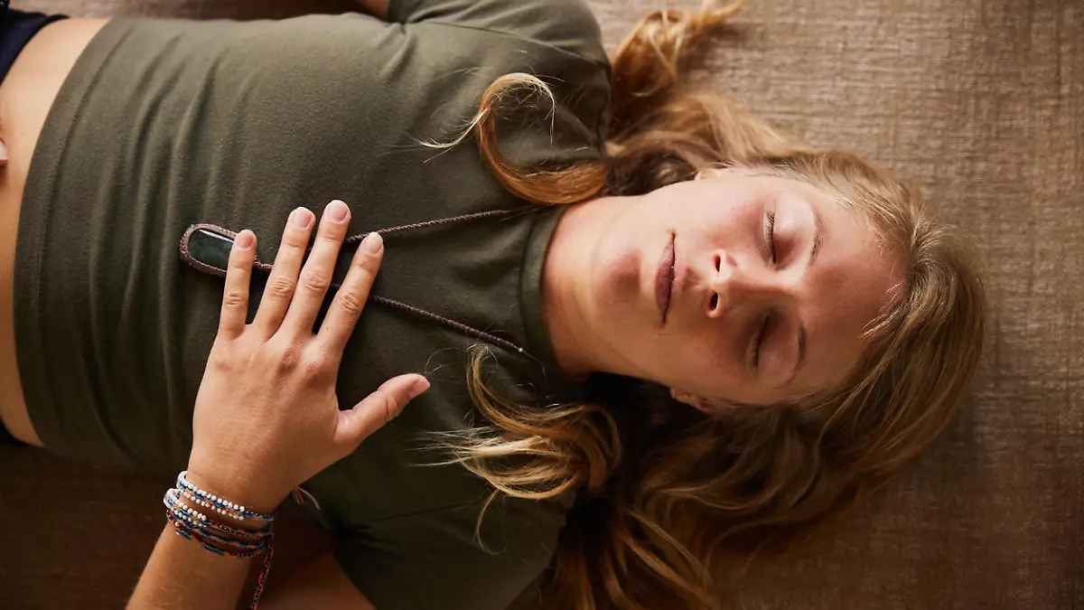 Young woman in sportswear doing breathing exercises while lying on an exercise mat on the floor of a studio during a yoga class