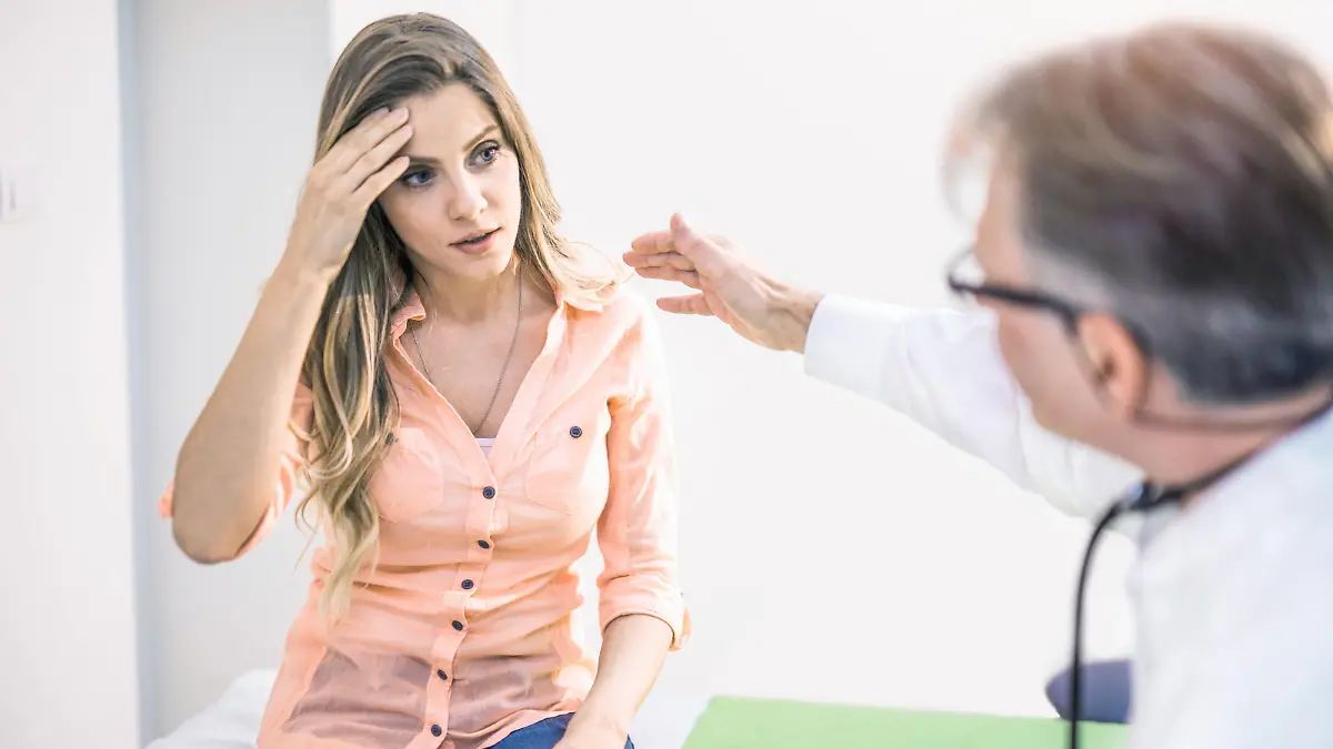 Young woman with a headache talking with her doctor.