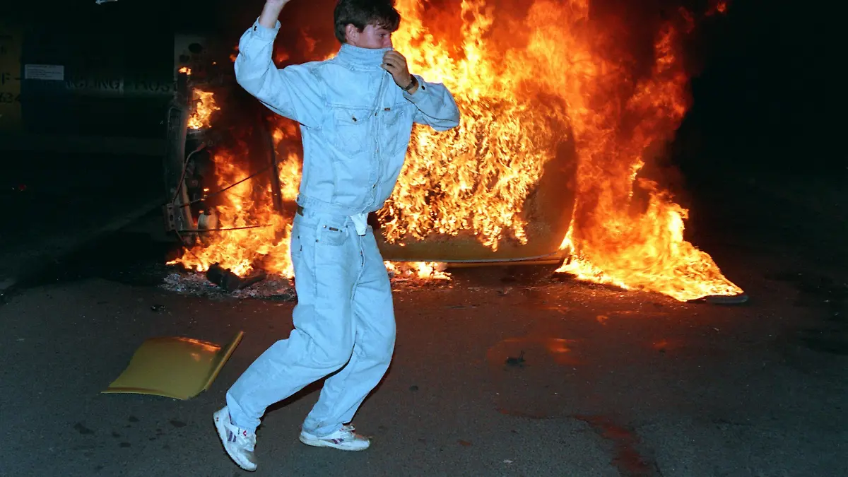 Vor einem brennendem Trabi wirft ein Randalierer am 26.8.1992 Steine auf Polizisten. Vom 22. bis 28. August 1992 randalierten bis zu 1200 meist jugendliche rechtsradikale Gewalttäter vor dem Zentralen Asylbewerberheim Mecklenburg-Vorpommern in Rostock-Lichtenhagen. Unter dem Beifall von bis zu 3000 Schaulustigen und vielen Fernsehkameras bewarfen die Rowdies das überwiegend mit Rumänen belegte Hochhaus sowie die Polizisten mit Steinen und Brandsätzen. Brandanschläge auf Ausländerwohnheime in Hoyerswerda und Rostock-Lichtenhagen warfen unmittelbar nach der Wende grelle Schlaglichter auf die rechte Szene im Osten. Doch die damals sichtbare Glut wurde nicht gelöscht, sondern glomm - oft im Verborgenen - weiter. In jüngster Zeit lodert sie immer häufiger empor. Kaum ein Tag vergeht im Osten Deutschlands ohne Meldungen über Straftaten mit rechtsextremistischem oder fremdenfeindlichem Hintergrund. Die Politik scheint hilflos, droht einerseits mit harten Strafen gegen die Gewalttäter und wiegelt andererseits wieder ab.