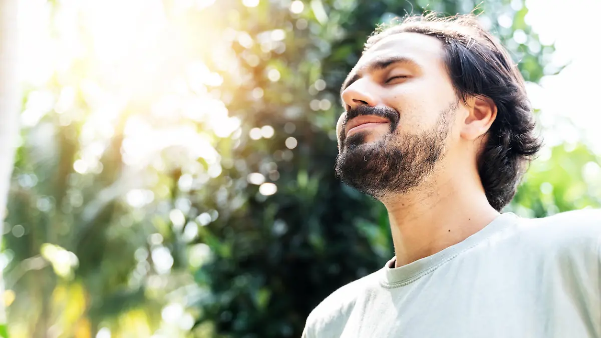 A bearded man is meditating outdoor in the park with face raised up to sky and eyes closed on sunny summer day. Concept of meditation, dreaming, wellbeing and healthy lifestyle