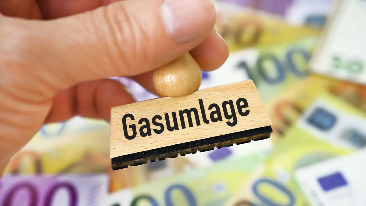 Hand hält Stempel mit Aufschrift Gasumlage vor Geldscheinen / action press