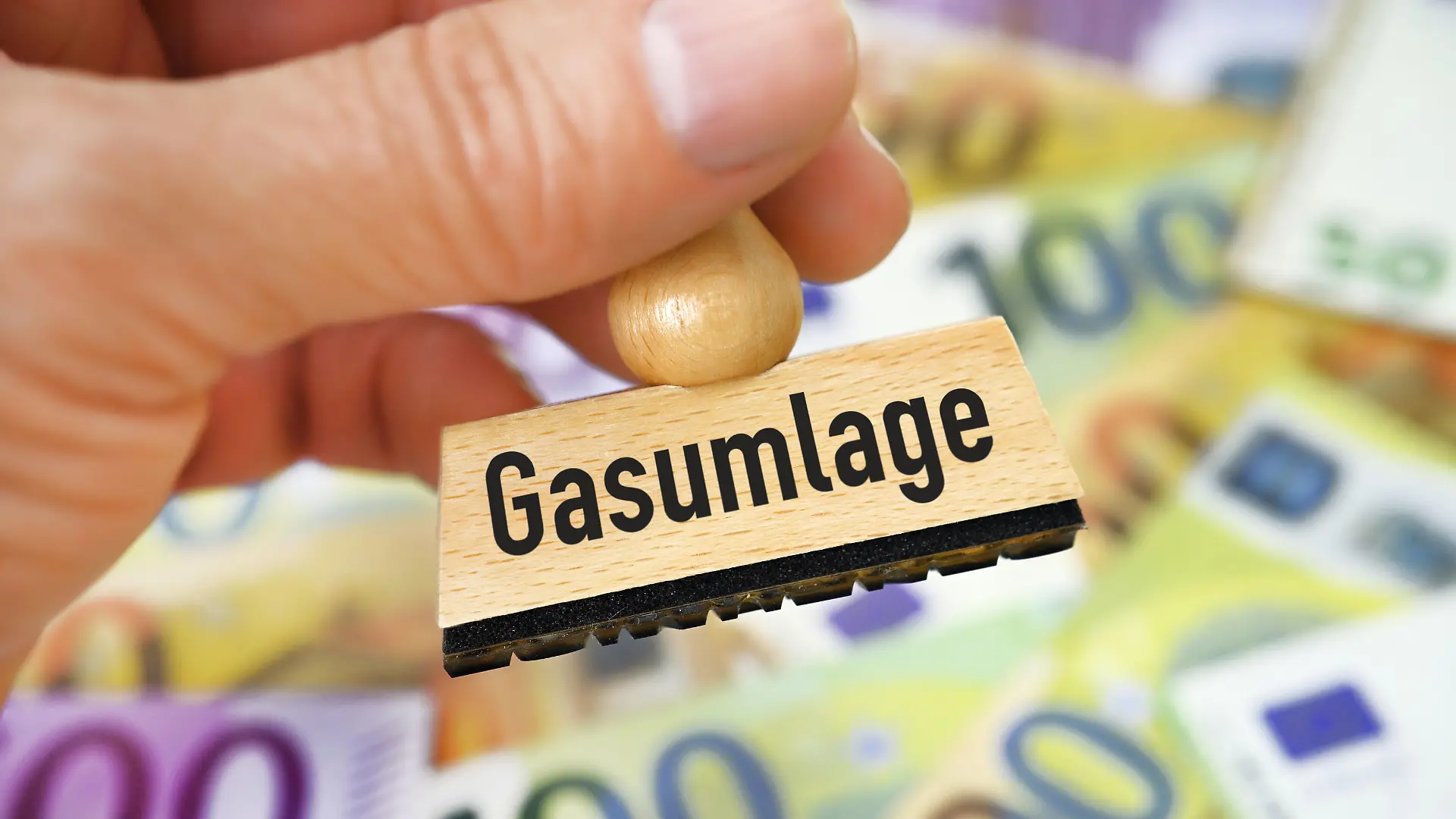 Hand hält Stempel mit Aufschrift Gasumlage vor Geldscheinen / action press