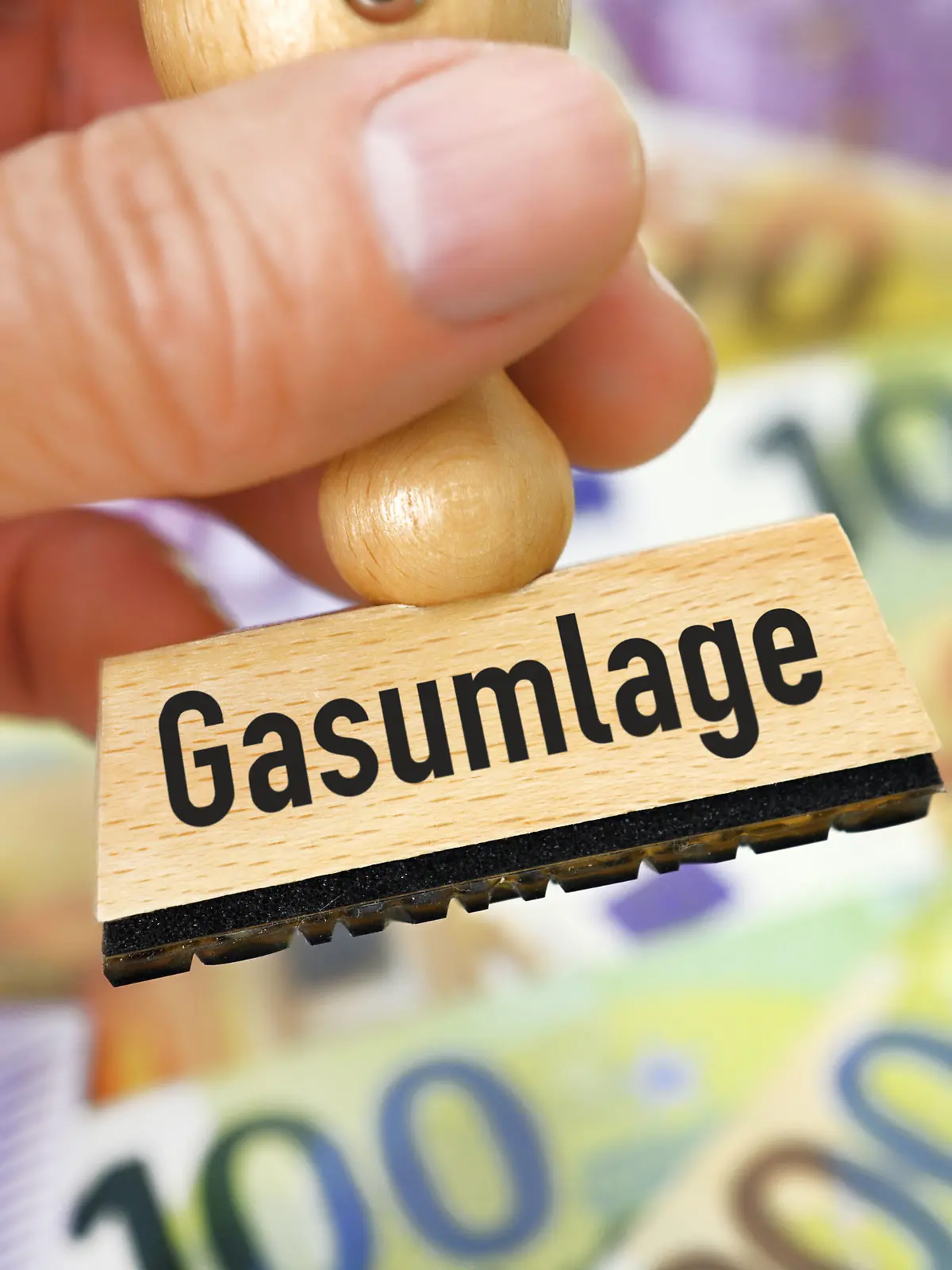 Hand hält Stempel mit Aufschrift Gasumlage vor Geldscheinen / action press