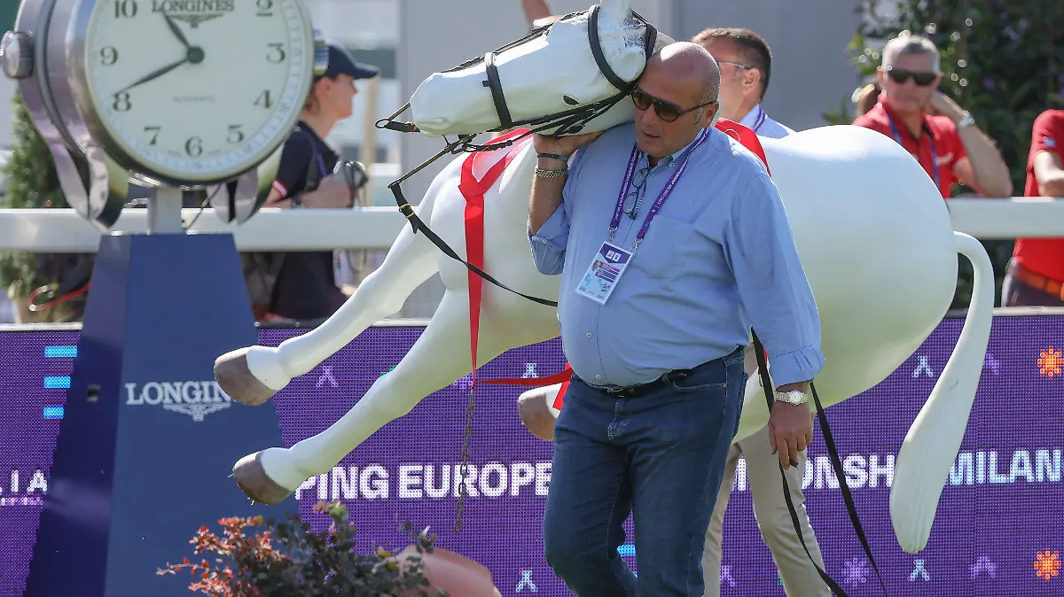 30.08.2023, Italien, Mailand: Pferdesport, Europameisterschaft, Springen, 1. Wertungsprüfung: Ein weißes Kunststoff-Pferd wird von zwei Helfern getragen. Der Reit-Weltverband FEI ließ zwei künstlichen Tiere aus dem Parcour entfernen, nachdem sie vor dem Start der Europameisterschaft in Mailand für Aufregung gesorgt hatten. Pferde würden durch solche Attrappen abgelenkt, so ein Reiter. Foto: Friso Gentsch/dpa +++ dpa-Bildfunk +++