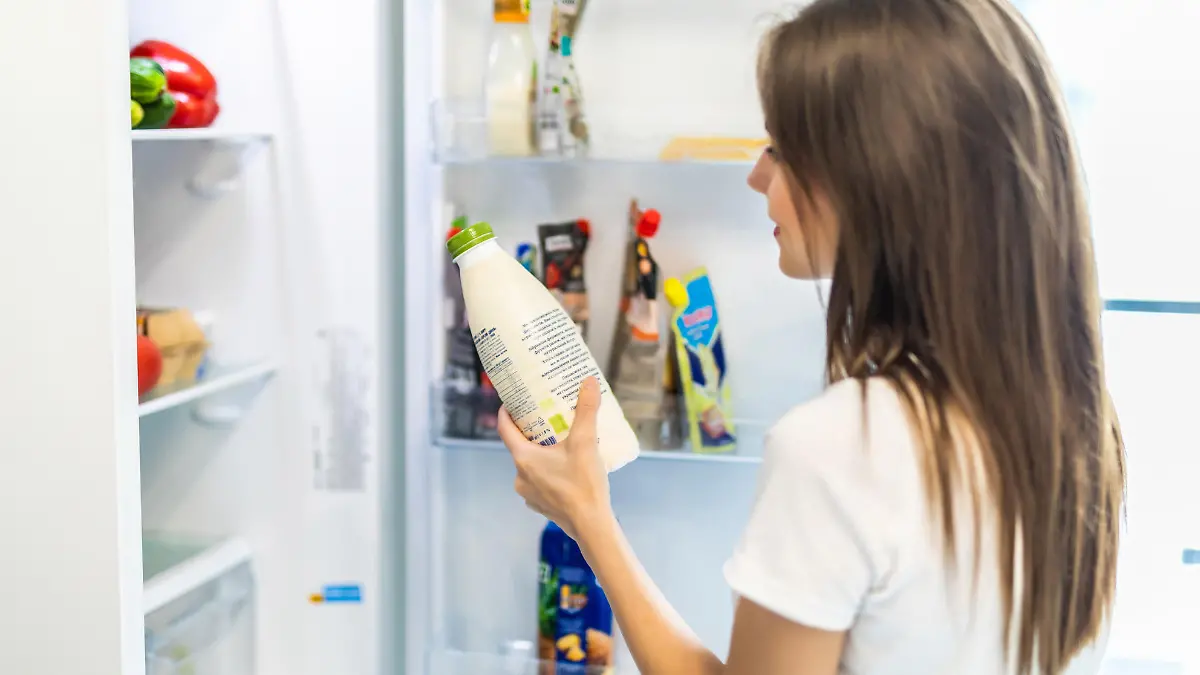 Woman chosen milk in opened refrigerator, cool new fridge full of tasty organic nutrition, female preparing to cook, healthy eating concept
