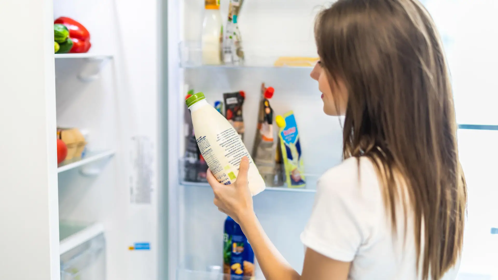Woman chosen milk in opened refrigerator, cool new fridge full of tasty organic nutrition, female preparing to cook, healthy eating concept