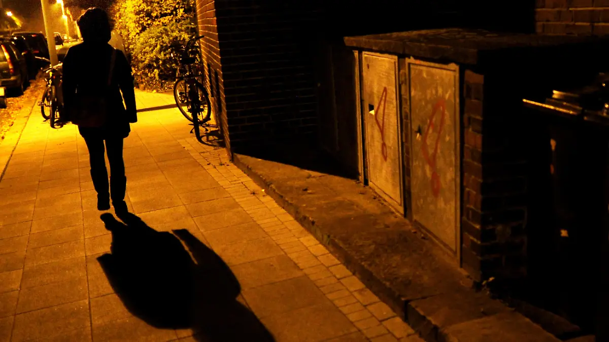 Eine Frau geht am 23.10.2012 im Licht der Straßenlaternen über eine Straße in Hannover und wirft einen langen Schatten. Foto: Julian Stratenschulte/dpa