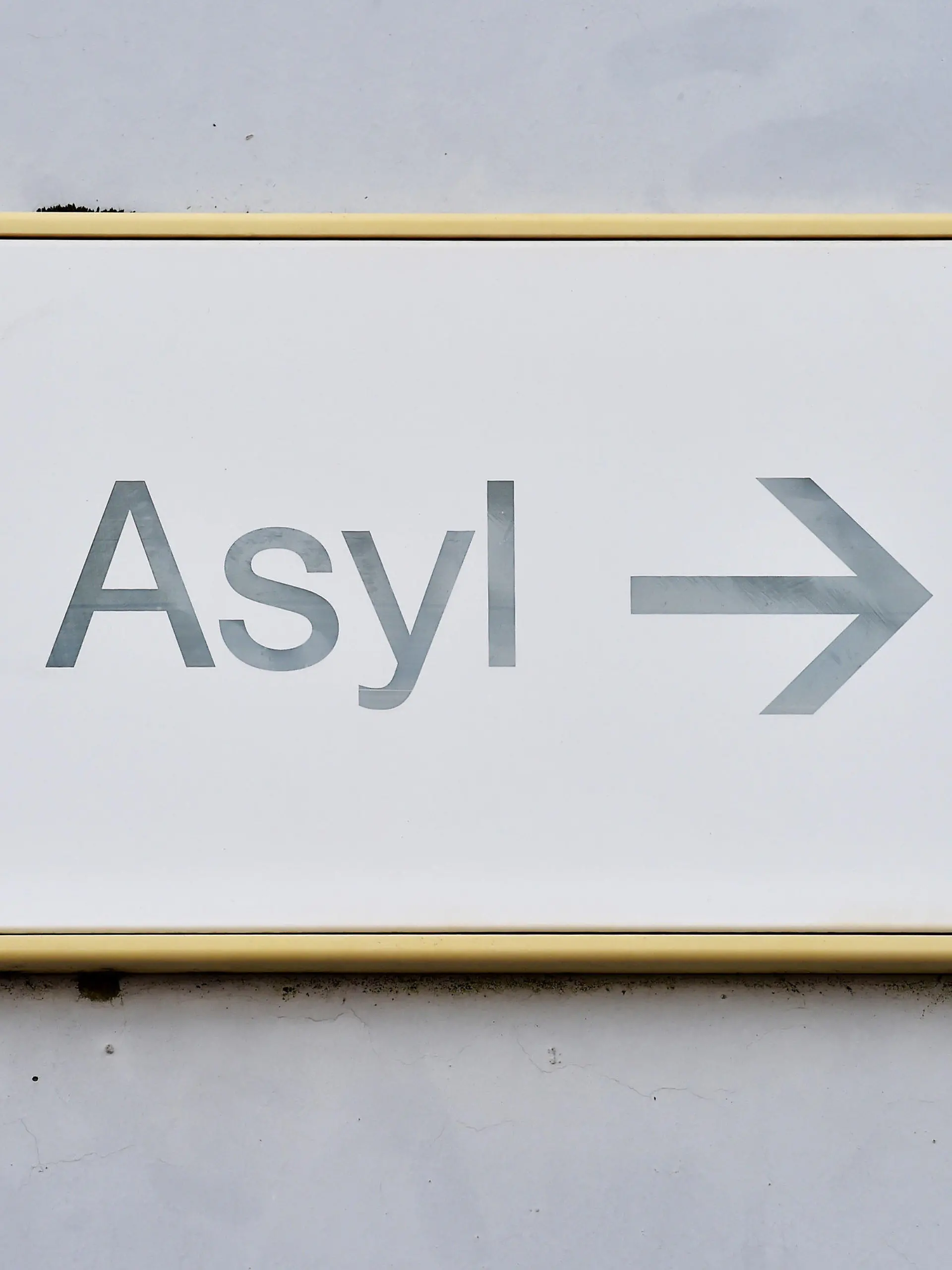 ARCHIV - 04.08.2014, Baden-Württemberg, Karlsruhe: Ein Schild mit der Aufschrift «Asyl» hängt in der Landeserstaufnahme für Asylbewerber (LEA) an einer Wand. Nach der scharfen Kritik an den Aussagen von Baden-Württembergs Ministerpräsident Winfried Kretschmann zum sogenannten Asylkompromiss erhält der Regierungschef parteiübergreifend Rückendeckung aus seinem Kabinett. (zu dpa: «Kretschmann bekommt Unterstützung im Streit um Asylkompromiss») Foto: Uli Deck/dpa +++ dpa-Bildfunk +++