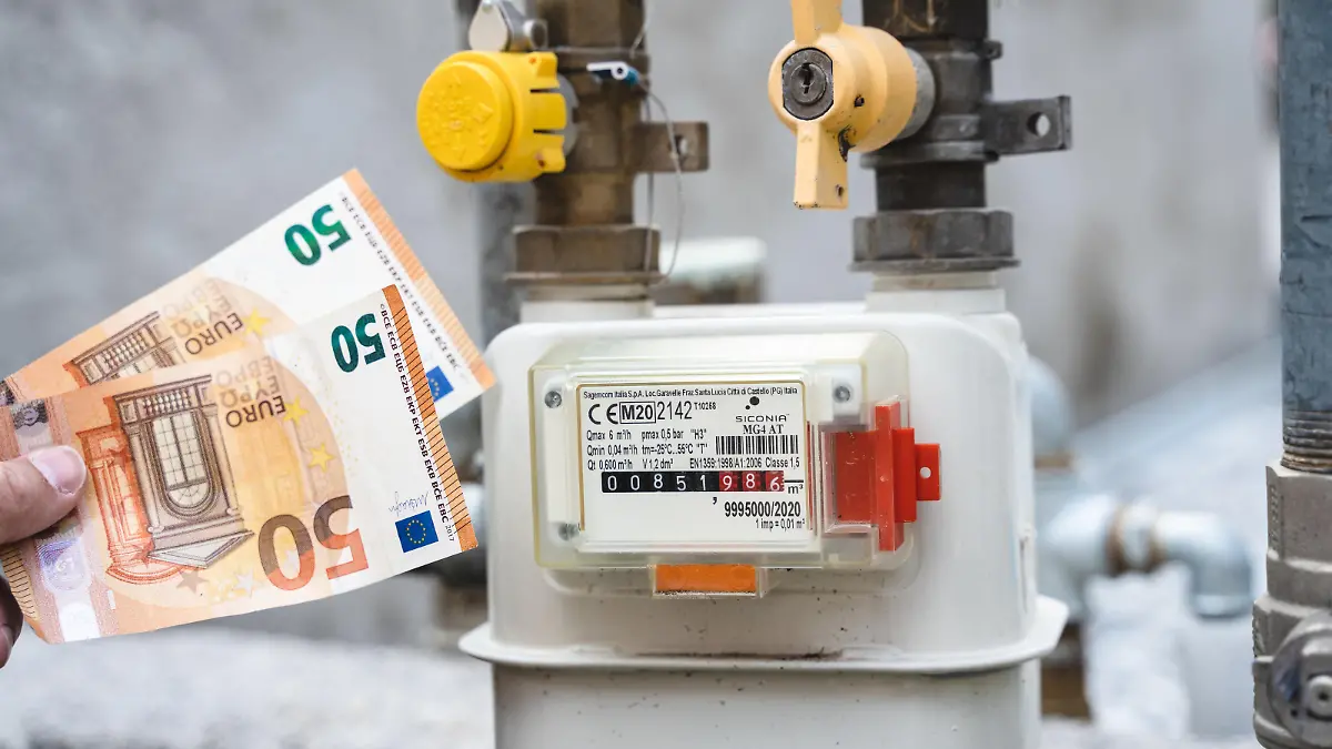 Riva, Trentino, Italy - 15 August 2022: Gas meter from a residential building outdoors. Male hand holding 50 euro bills in front of gas meter and pipe, symbolic image rising cost of electricity, gas and energy *** Gaszähler von einem Wohnhaus im Freien. Männliche Hand hält 50 Euro Geldscheine vor Gas Zähler und Leitung, Symbolbild steigende Kosten für Strom, Gas und Energie
