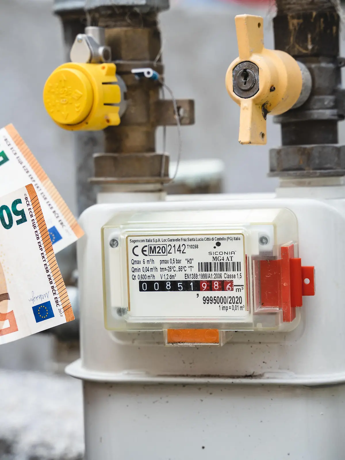 Riva, Trentino, Italy - 15 August 2022: Gas meter from a residential building outdoors. Male hand holding 50 euro bills in front of gas meter and pipe, symbolic image rising cost of electricity, gas and energy *** Gaszähler von einem Wohnhaus im Freien. Männliche Hand hält 50 Euro Geldscheine vor Gas Zähler und Leitung, Symbolbild steigende Kosten für Strom, Gas und Energie