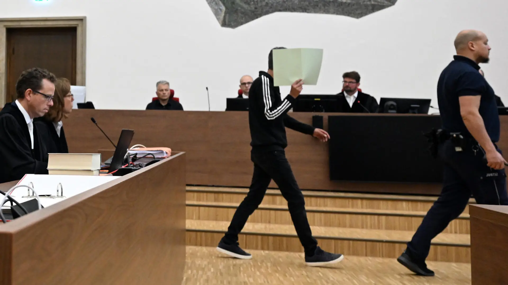 Bernhard Günther (l), ehemaliger Finanzchef von Innogy, und sein Rechtsanwalt Martin Meinberg (M) schauen zu, wie der Angeklagte in den Gerichtssaal geführt wird. Mehr als vier Jahre nach dem Säureanschlag auf Günther beginnt in Wuppertal der Prozess gegen einen der mutmaßlichen Attentäter. Der 42-jährige Belgier war im vergangenen Dezember in der belgischen Provinz Limburg festgenommen worden.