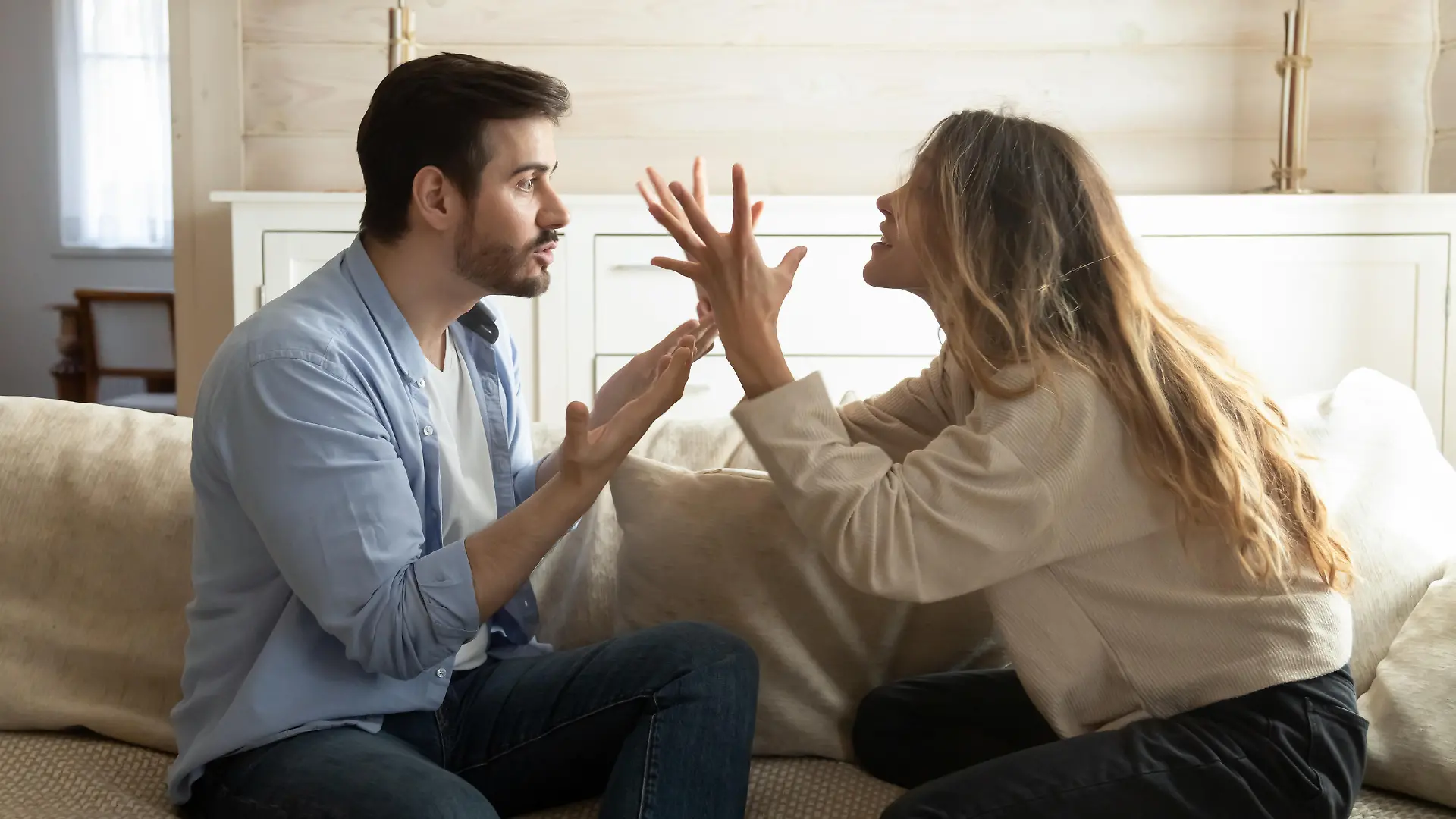 Emotional annoyed stressed couple sitting on couch, arguing at home. Angry irritated nervous woman man shouting at each other, figuring out relations, feeling outraged, relationship problems concept.