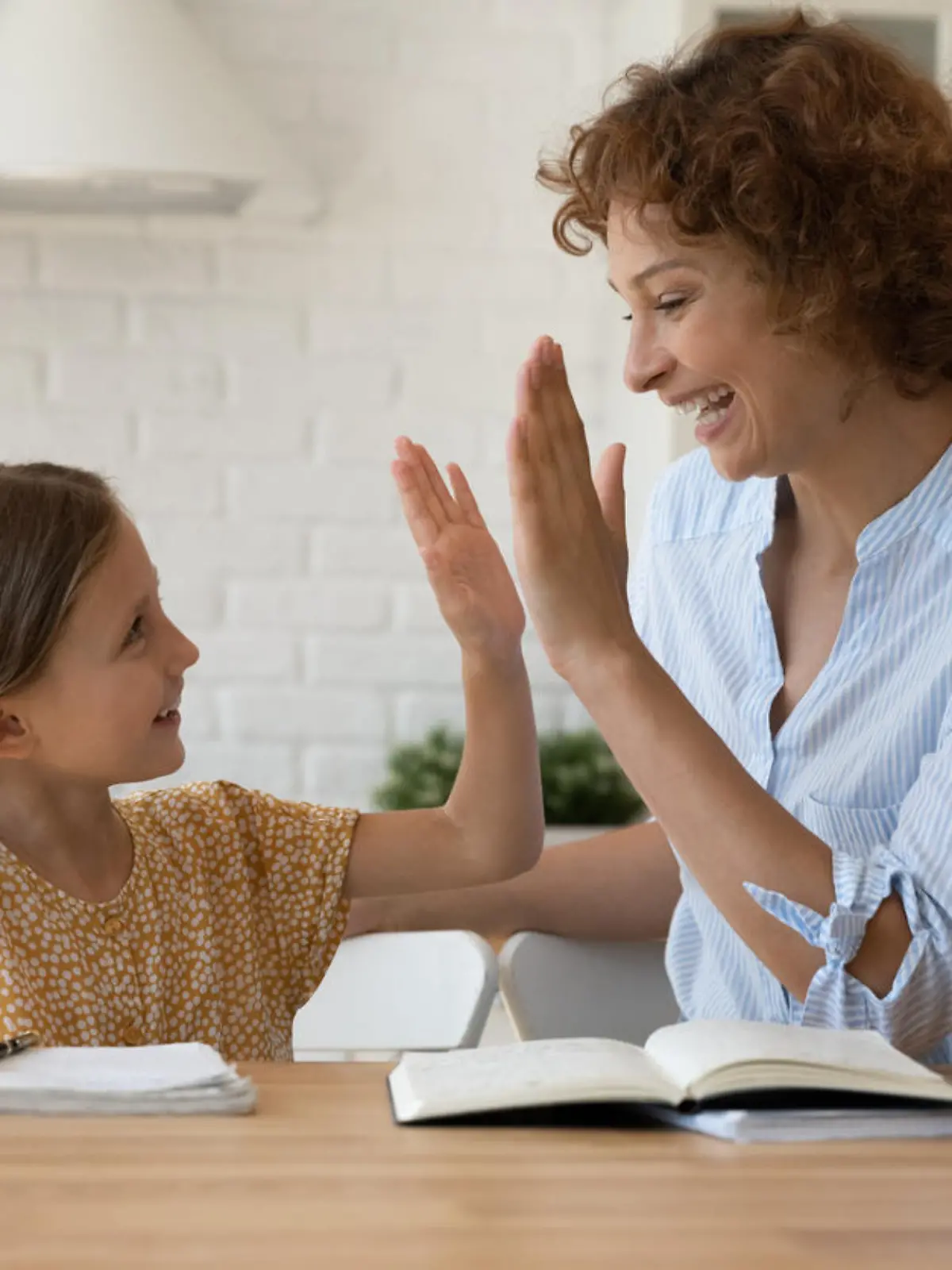 Well done dear. Excited mother give high five to small daughter praise child for reaching success in homework. Joyful female tutor greet schoolgirl for giving correct answer solving hard math problem